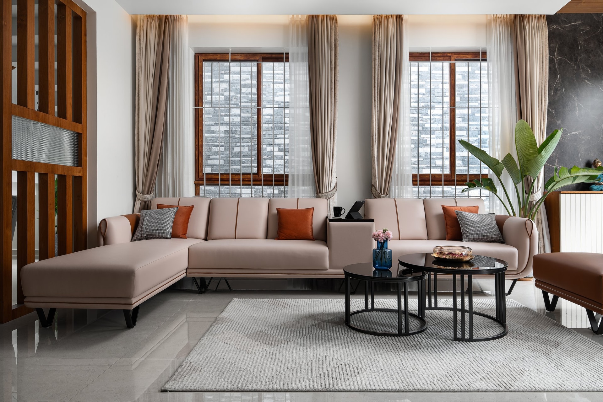 The living room, where a long blush sectional and twin stone-clad windows establish the home's matte-and-warm vocabulary