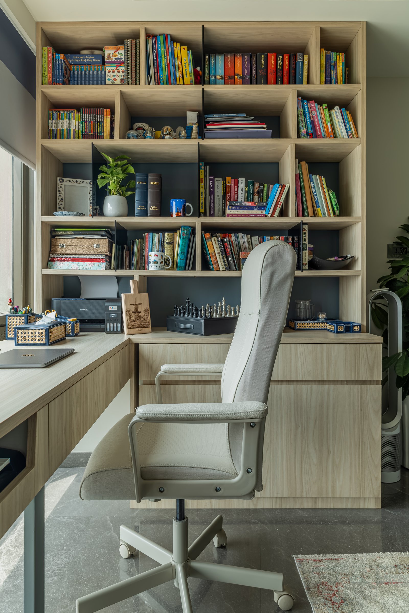 The study, built around a pale-wood L-shaped desk and a tall open bookshelf backed in slate-blue