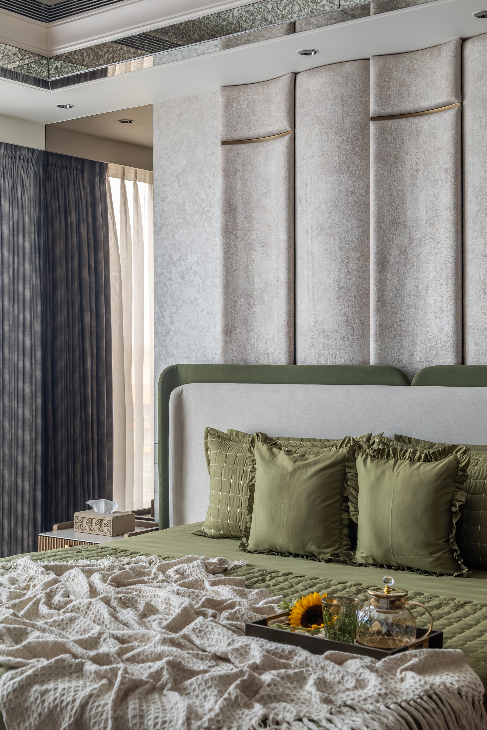 The principal bedroom, where a floor-to-ceiling upholstered wall in soft taupe rises behind the bed