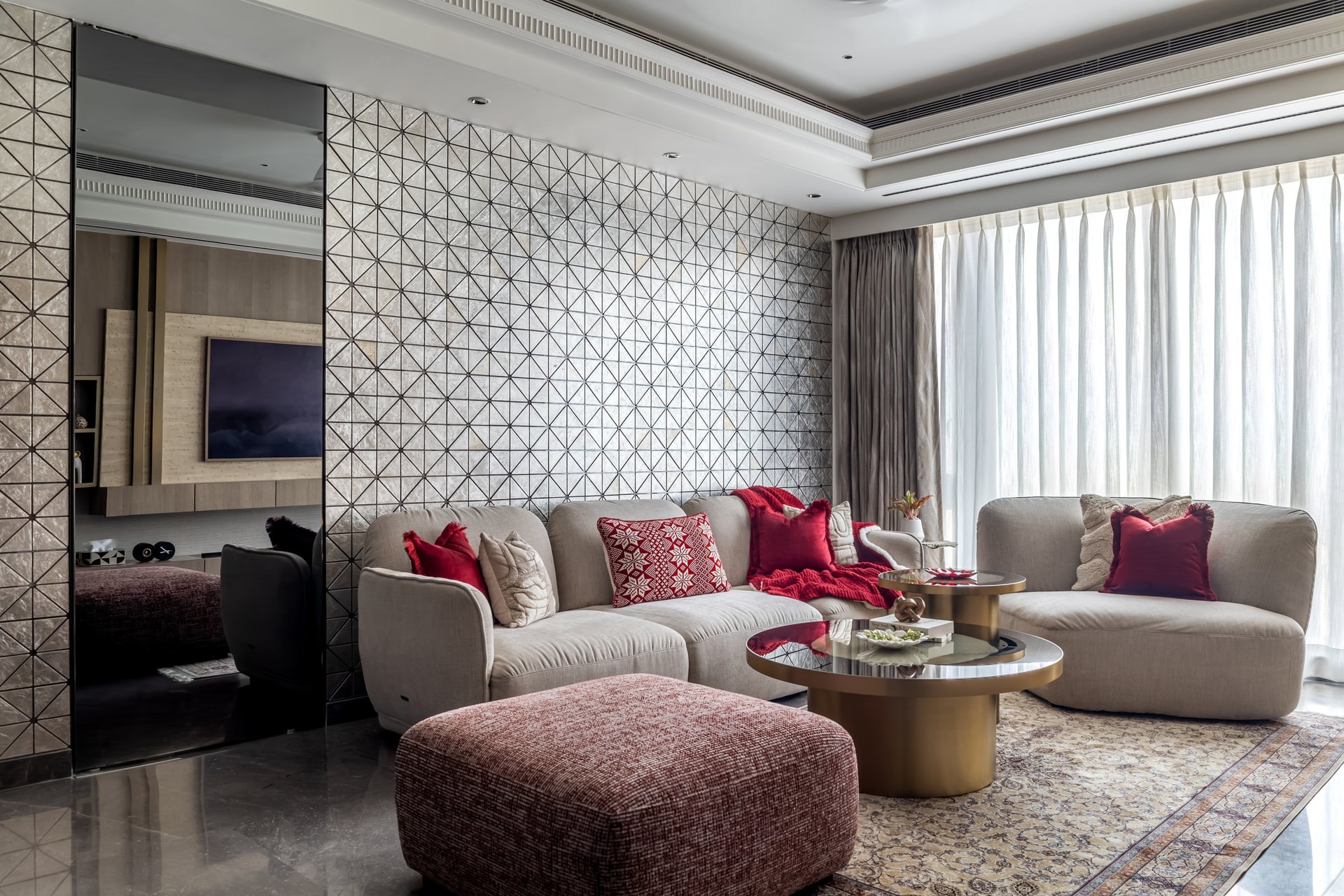 The living room, where a triangular mirrored wall fragments daylight behind a curved linen sofa