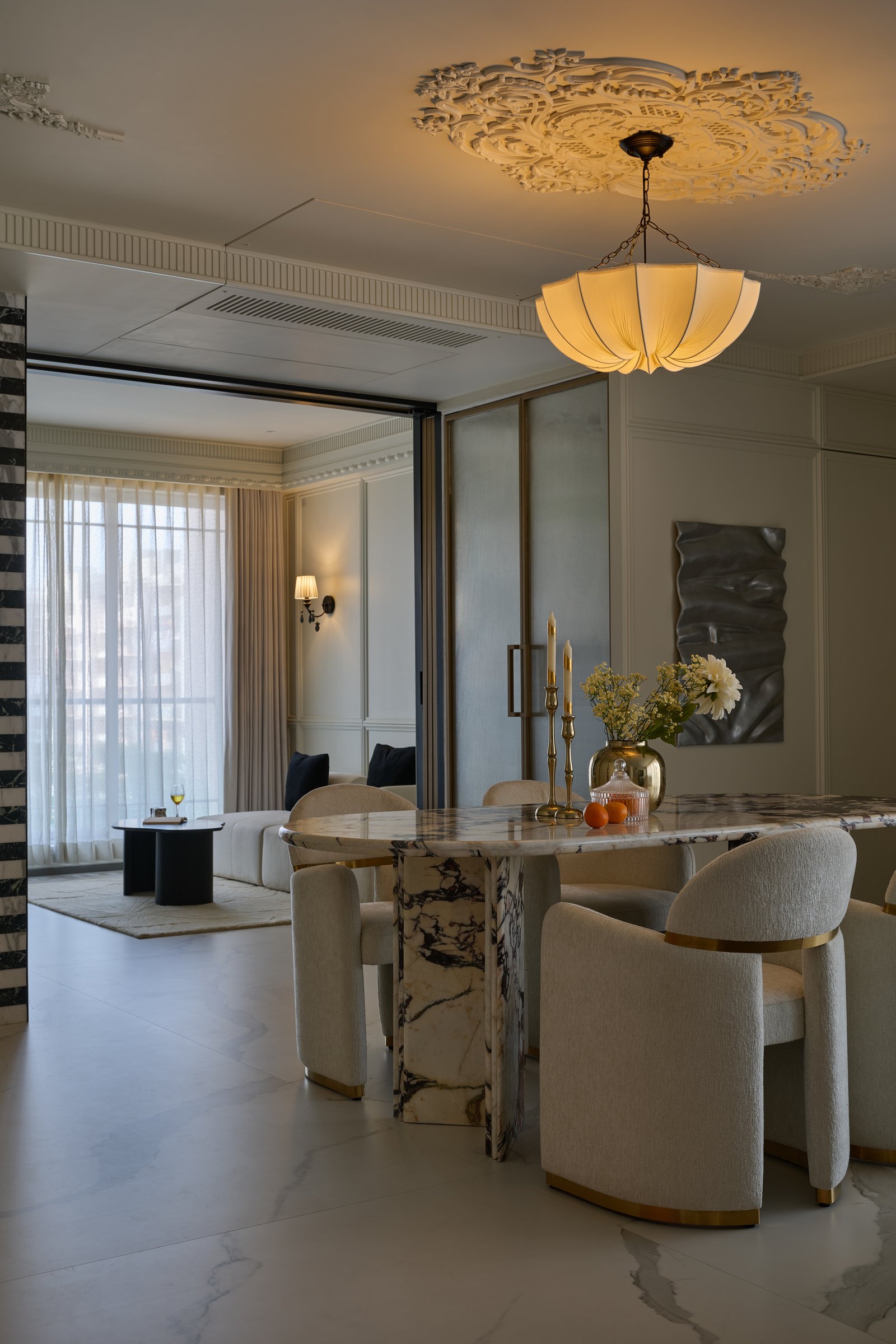 The dining area, anchored by a heavily veined marble table and boucle chairs with brass-banded bases