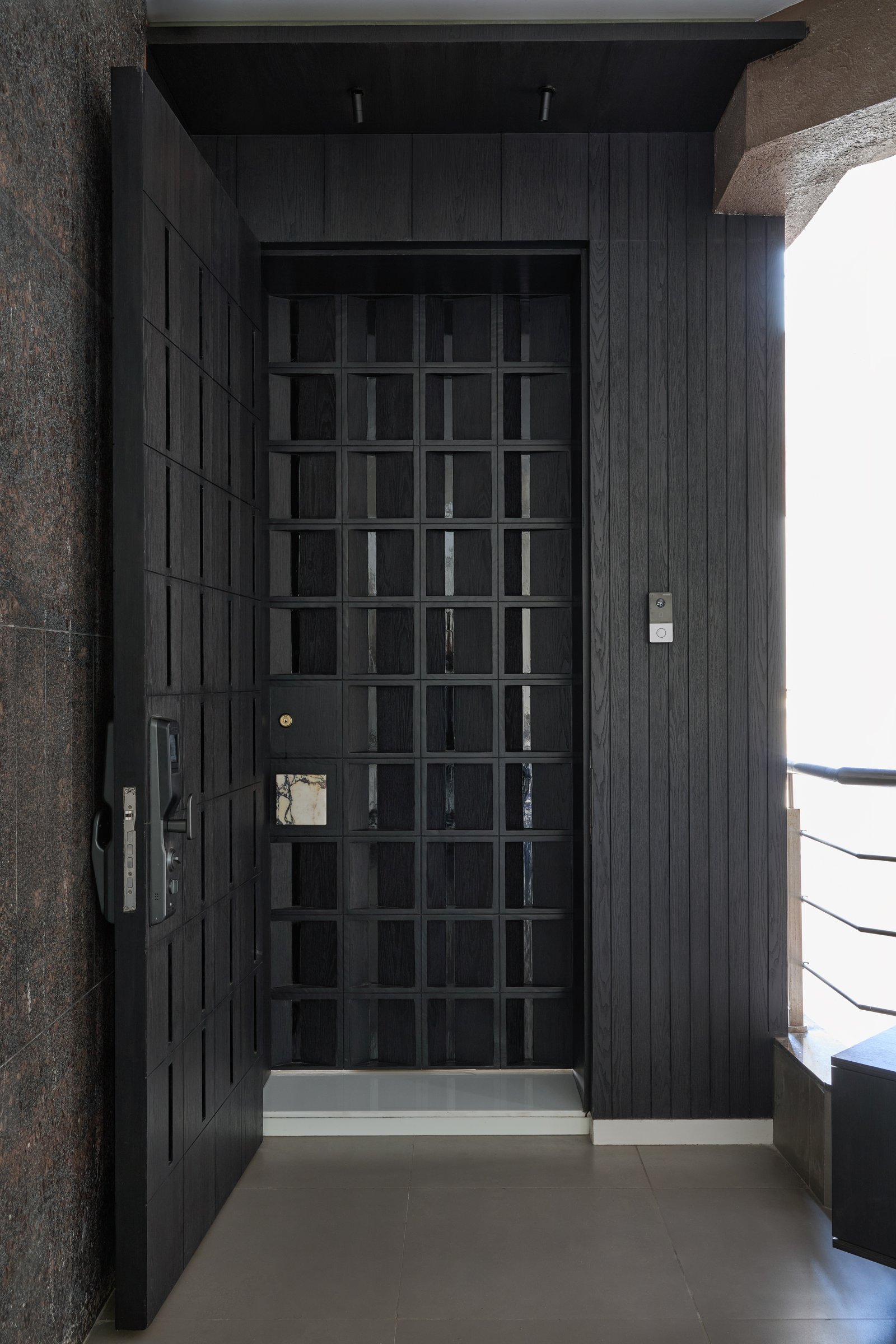 The entry: a dark grid door with a single inset of veined marble, framed by vertical board cladding in the same tone