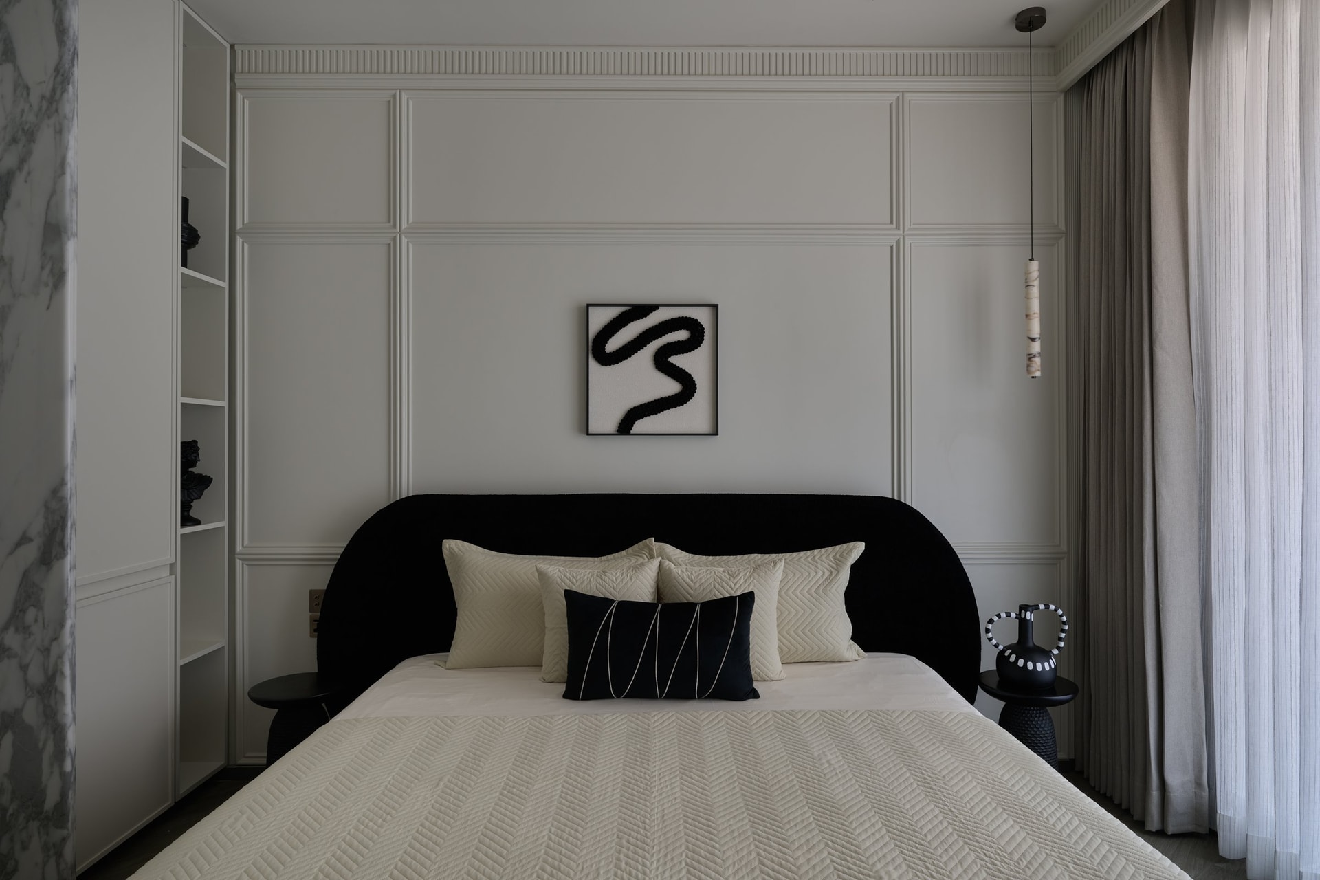 Another bedroom, where a deeply curved black upholstered headboard anchors the panelled wall