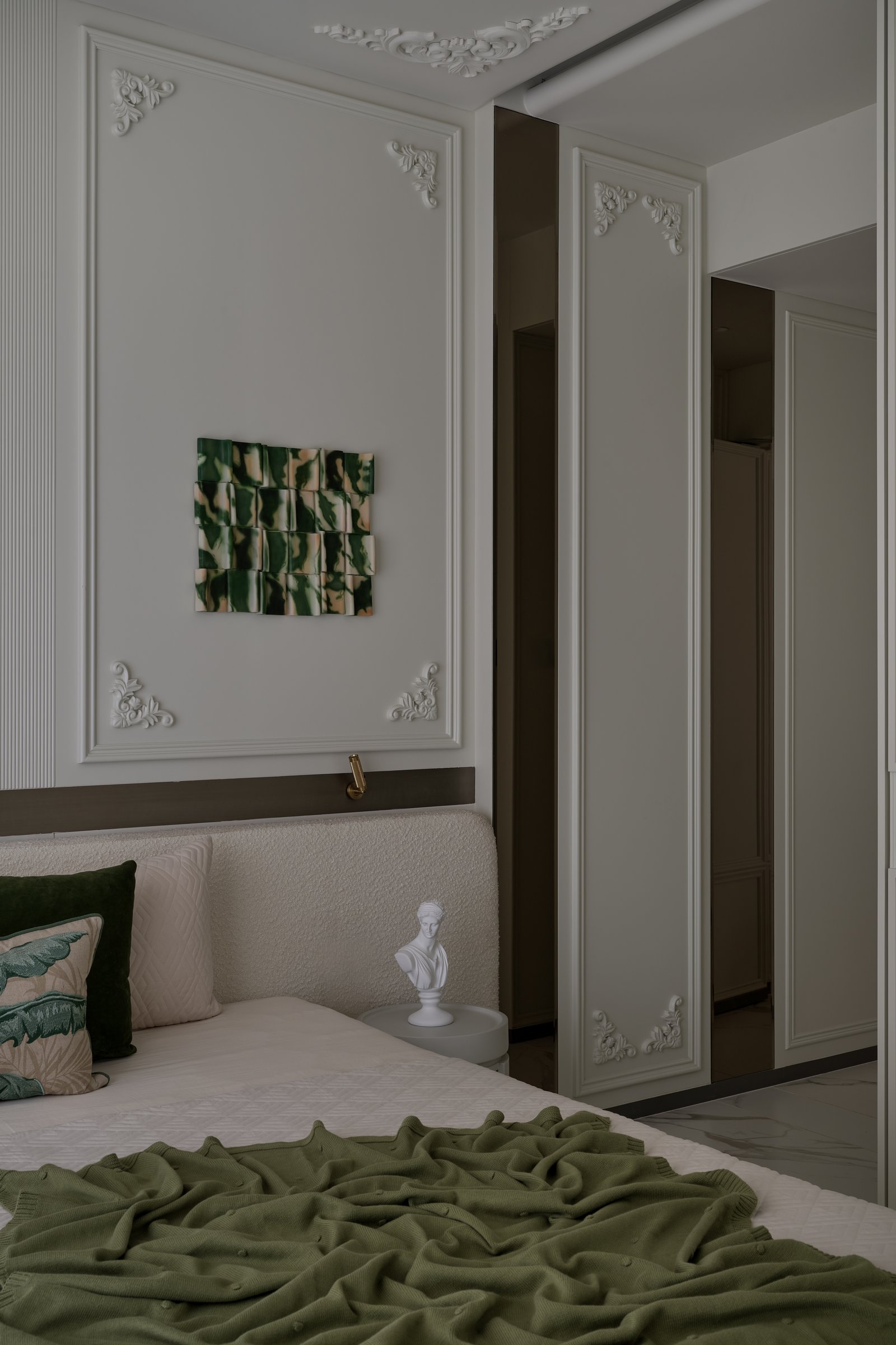 The room from the opposite side, where a mirrored wardrobe wall doubles the green ceramic artwork in reflection