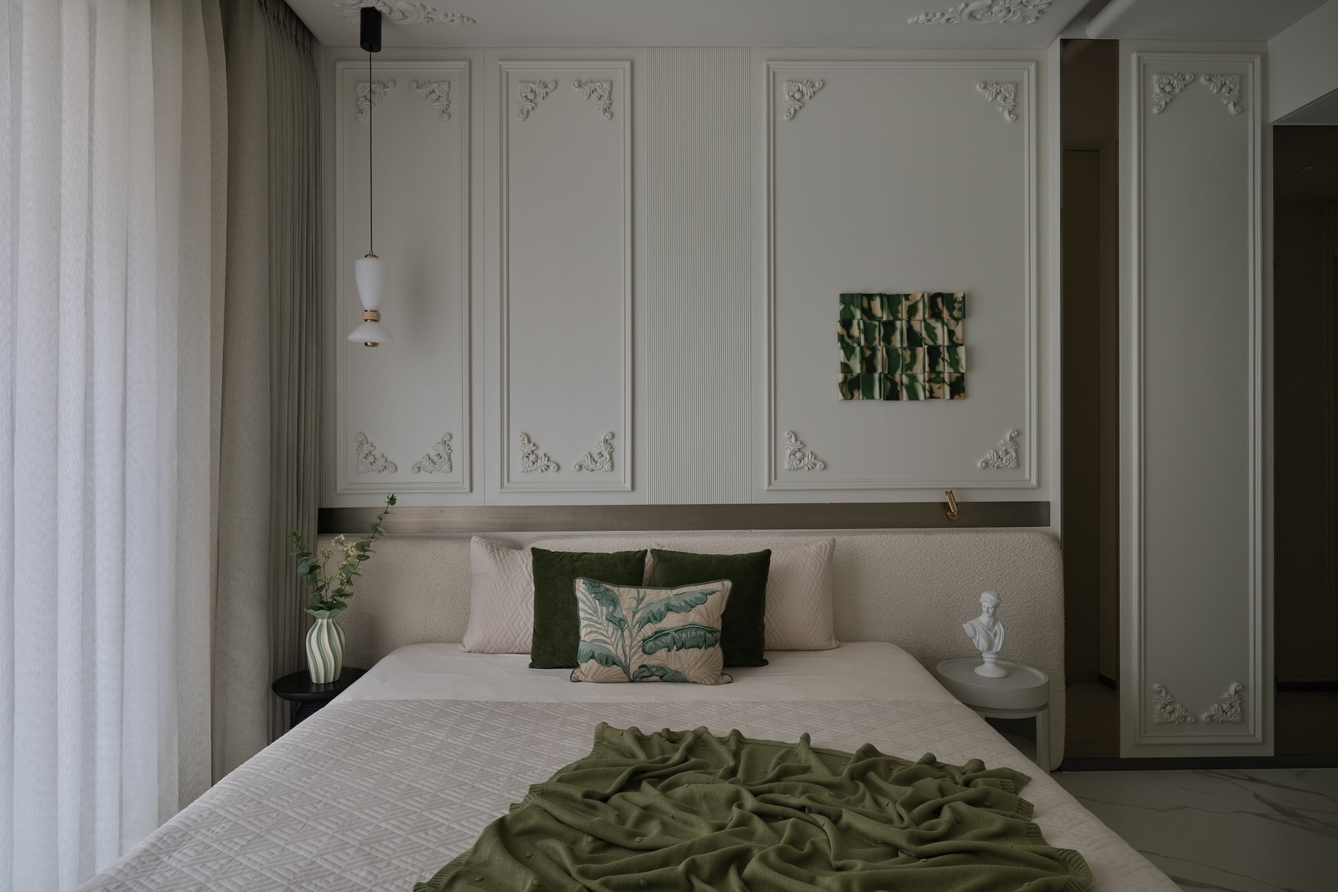 The primary bedroom, where panelled mouldings frame a boucle headboard and a green ceramic tile artwork