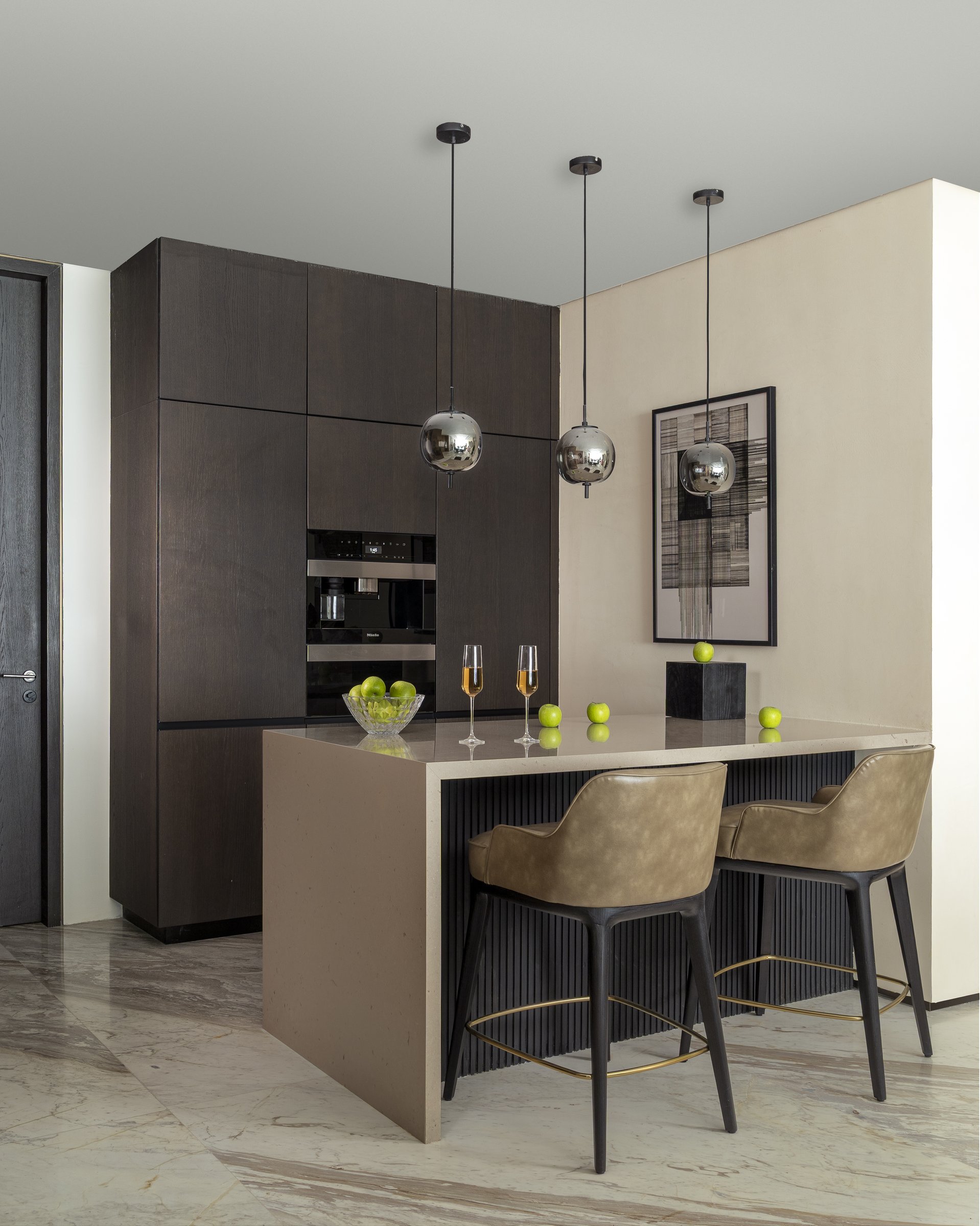 The kitchen island in pale stone, set against deep coffee-brown cabinetry and three smoked glass pendants