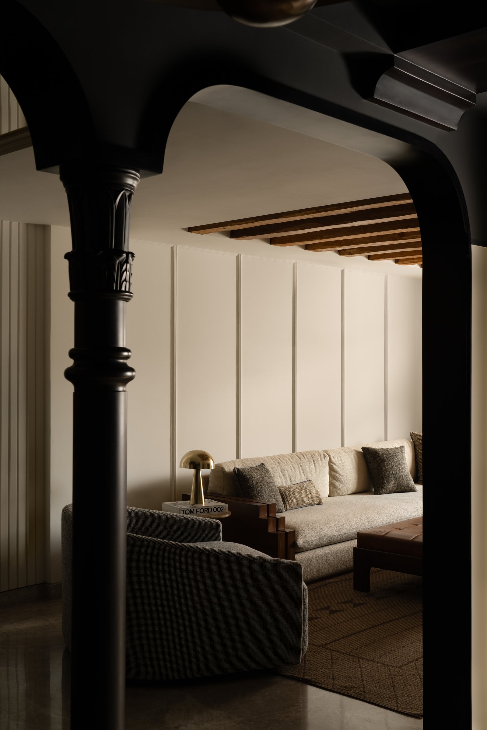 The living room seen through one of the home's defining black arches, framing a dialogue between dark structural ornament and pale upholstered softness