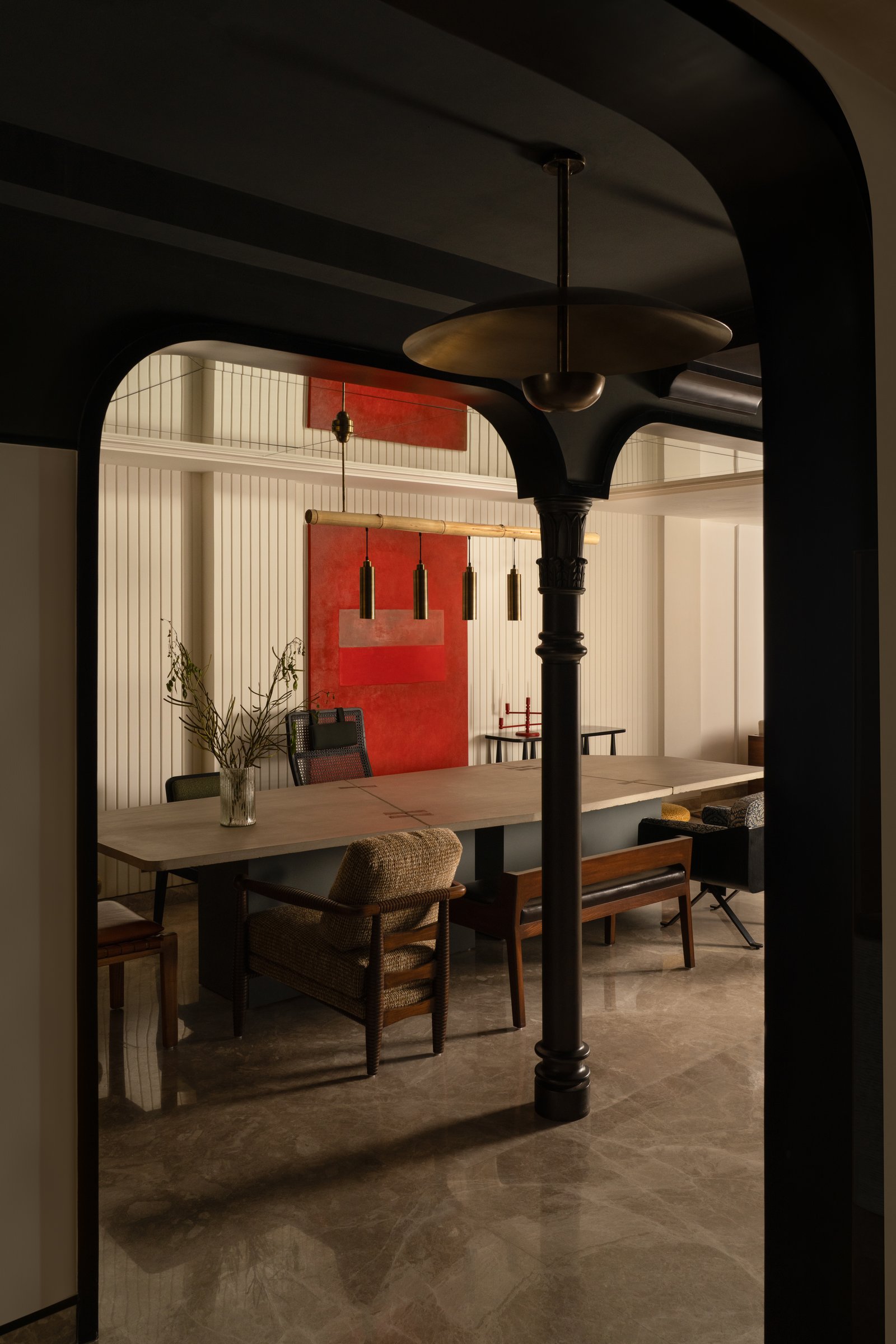 The dining area, anchored by a four-metre concrete table and a bamboo-and-brass linear pendant, with a red abstract canvas reinforcing its theatricality