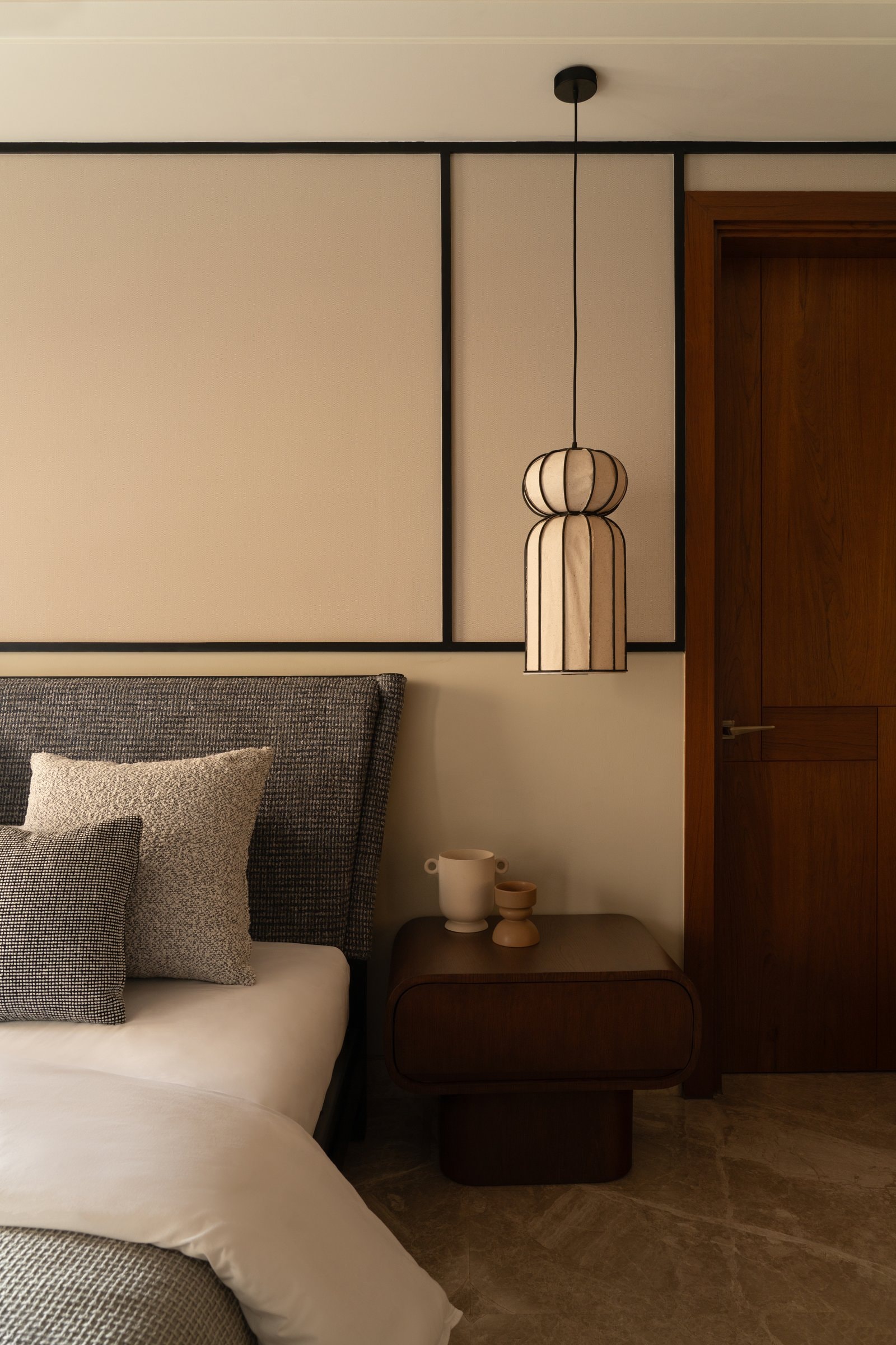 A second bedroom, where an upholstered wall divided by black framing carries a single fabric pendant beside the bed