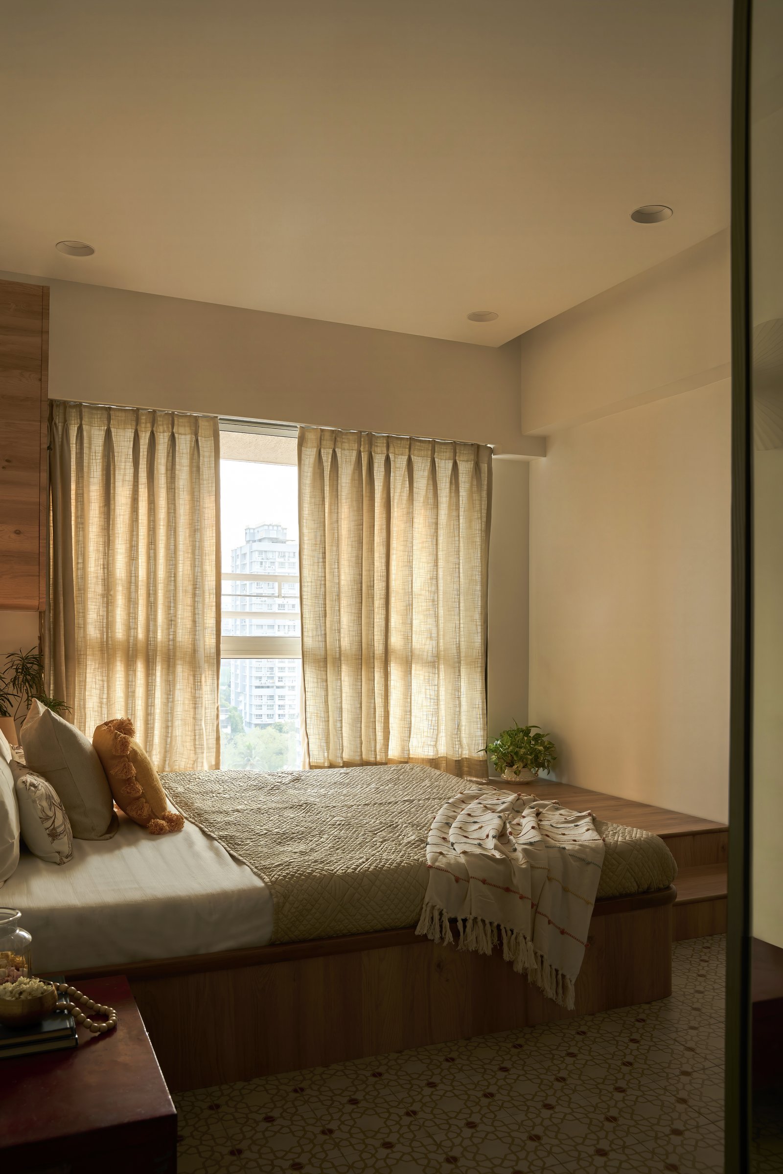 The bed extends into a raised timber platform running to the window, doubling as a low seat and a plinth for greenery