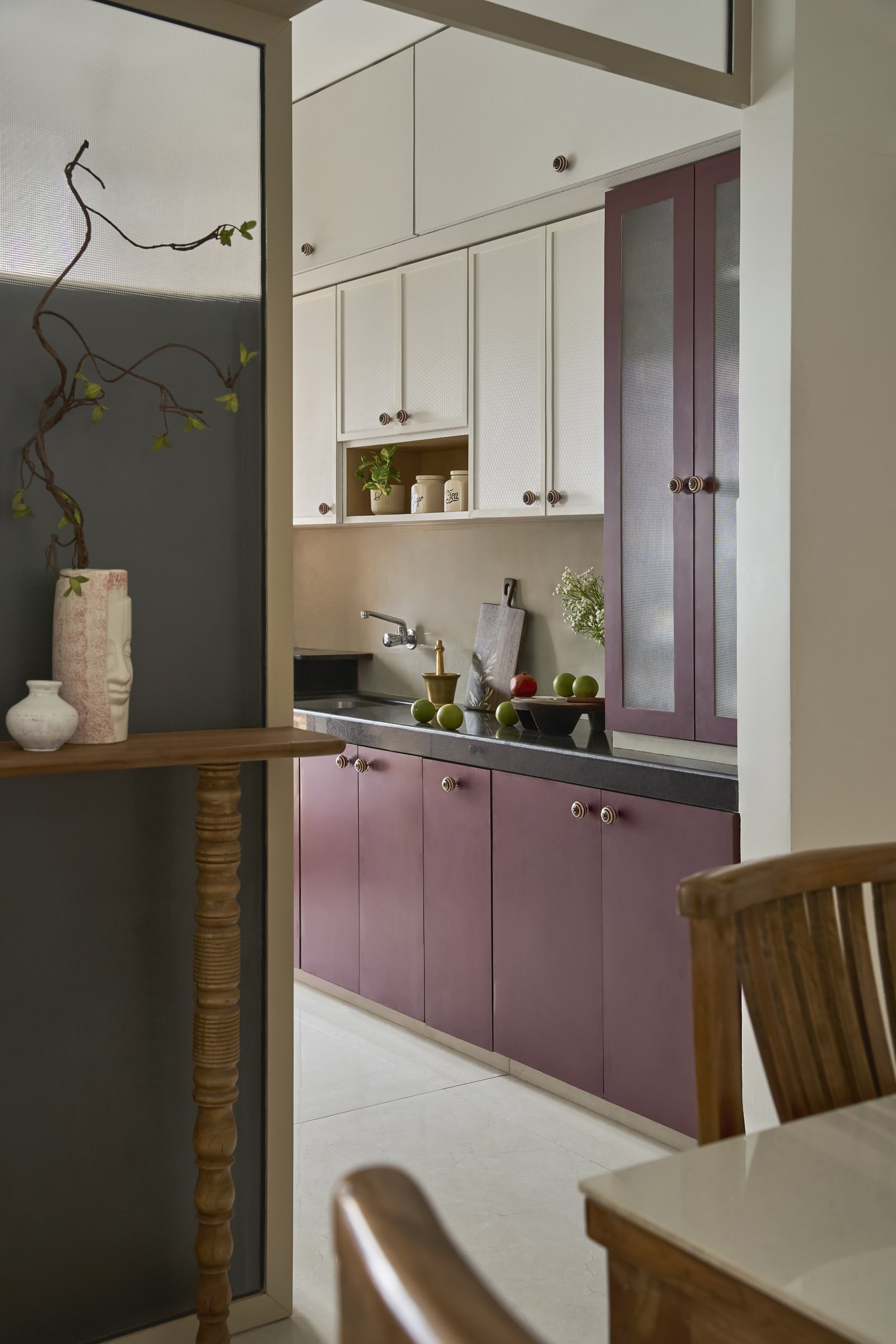 The galley kitchen, where muted plum cabinetry meets soft cream uppers and a dark stone counter