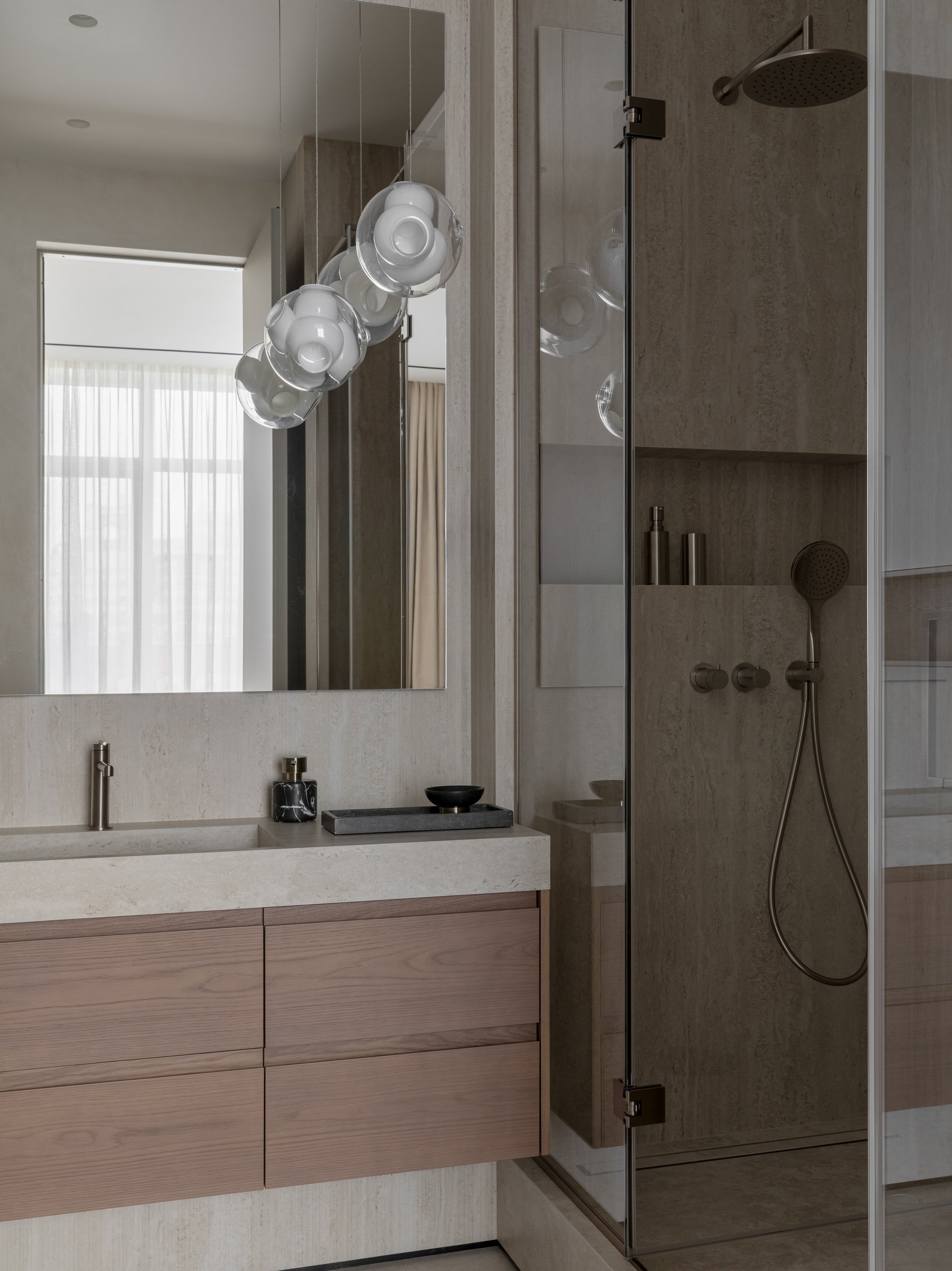 The shower zone, where stone-clad walls and brushed fittings continue the vanity's material vocabulary
