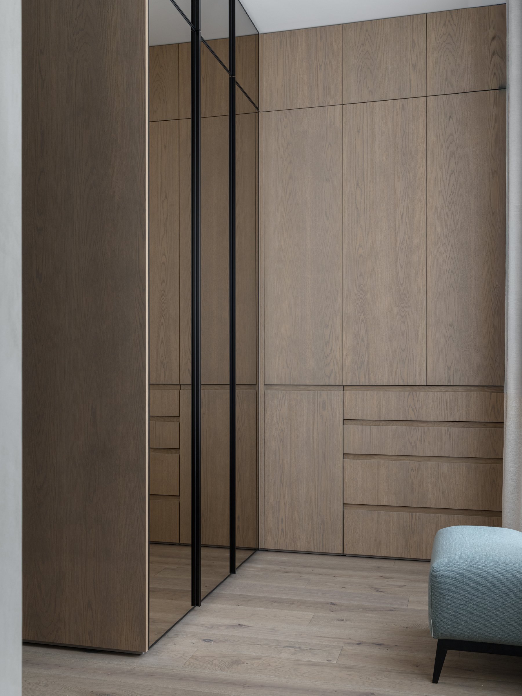 The dressing area, where full-height oak cabinetry meets a mirrored panel that lengthens the volume