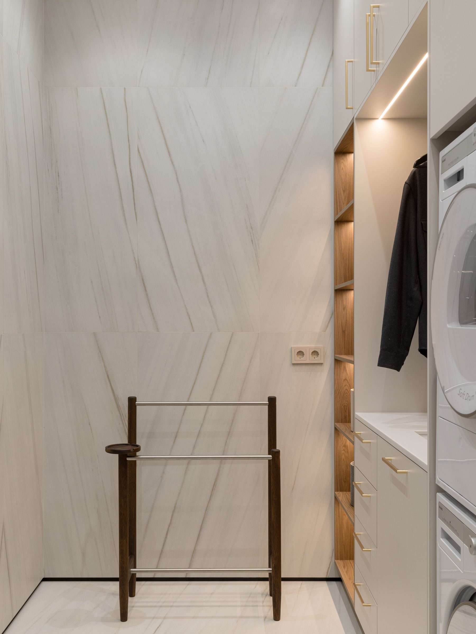 The laundry room, where white-veined stone meets pale cabinetry and a slender wooden valet stand