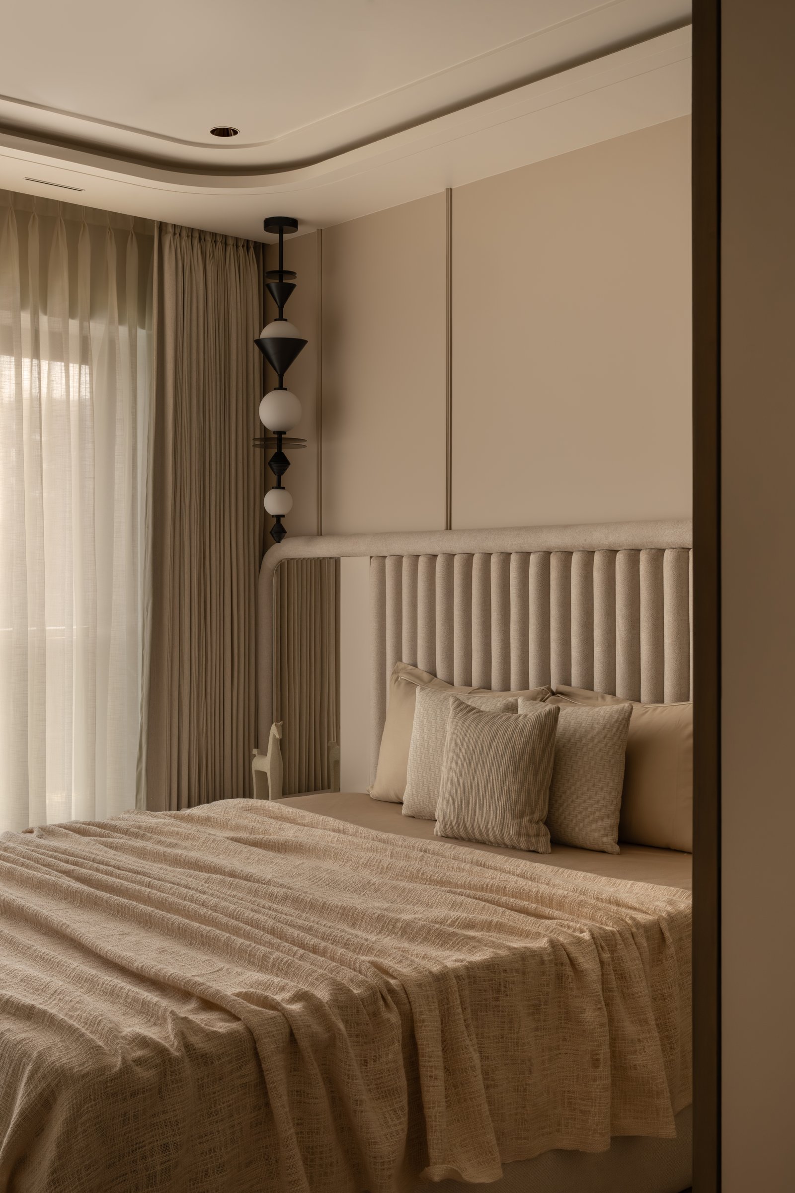 The guest bedroom, where a fluted upholstered headboard and a vertical composite pendant establish a quieter register
