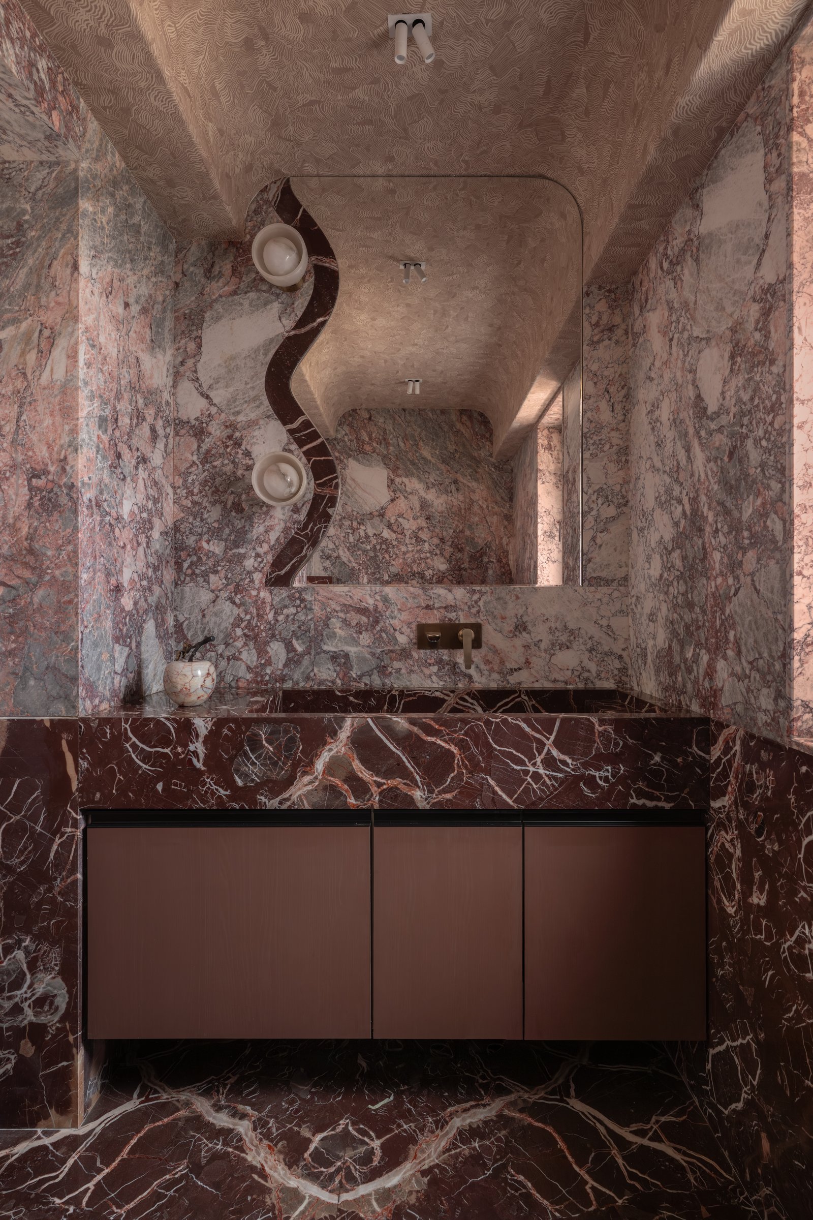 The powder room, where richly veined burgundy marble creates a cavernous, immersive volume
