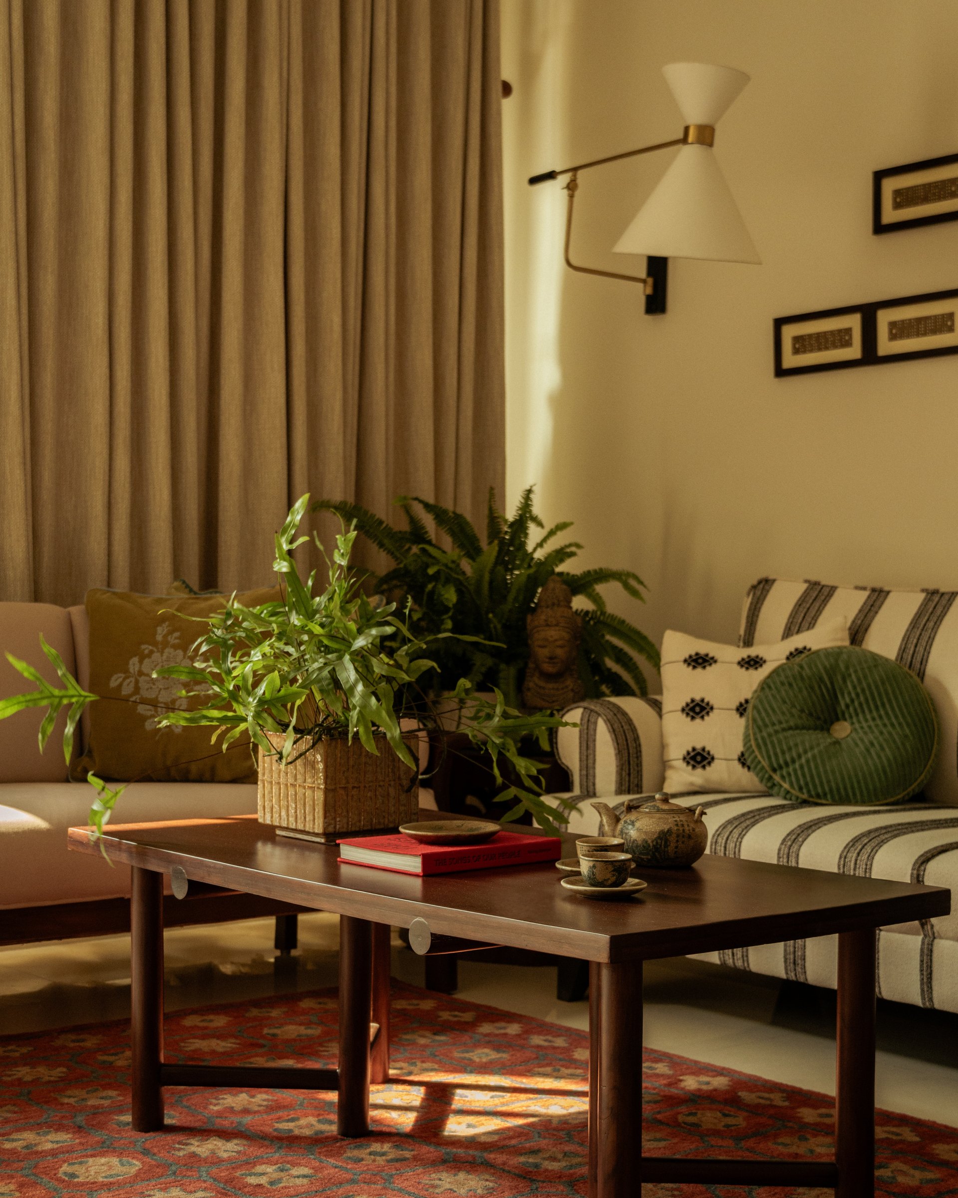 The living room, where a striped upholstered sofa, a low dark-wood coffee table, and framed handloom punch cards establish the home's material palette