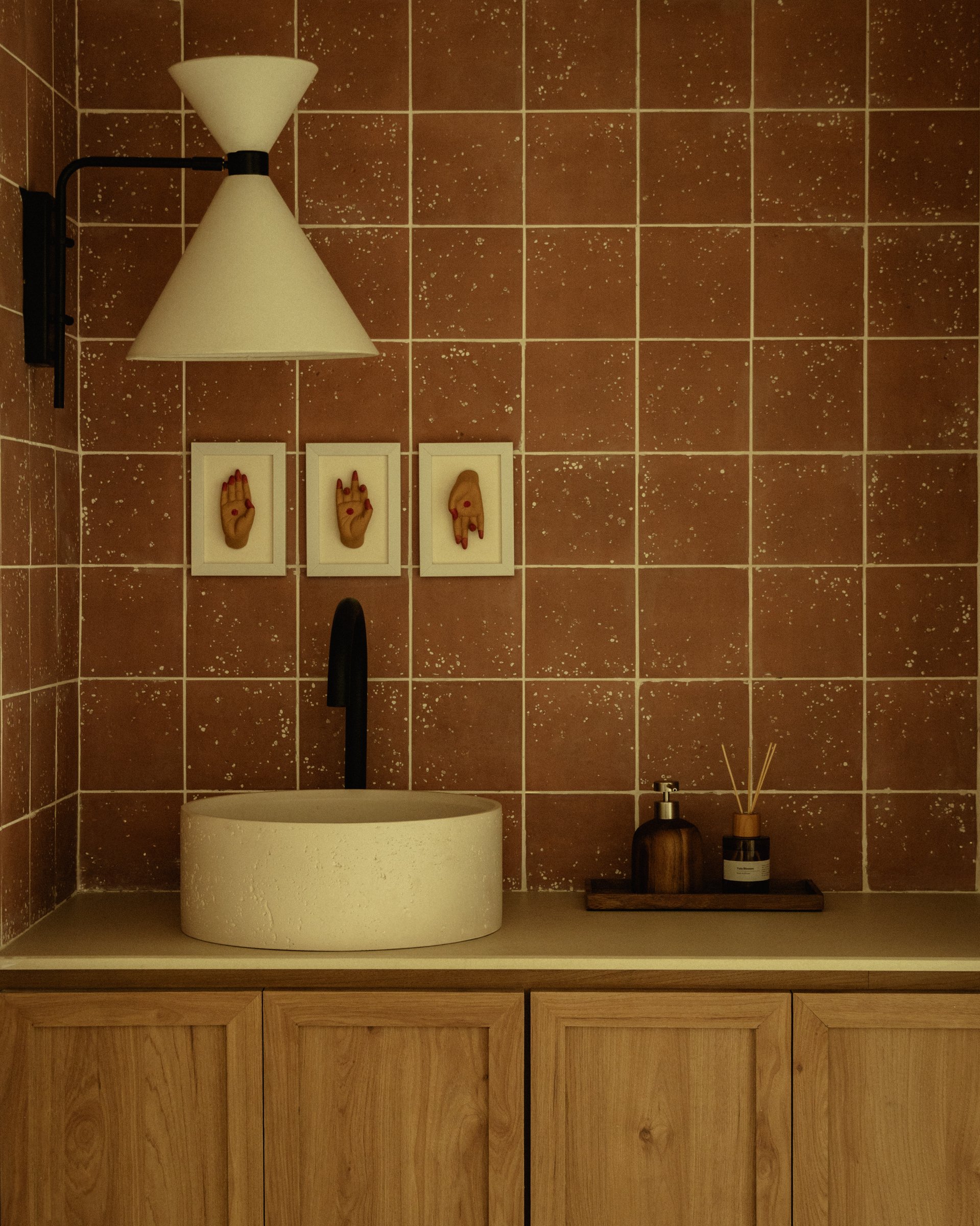 The powder room, where terracotta-toned speckled tiles hold three small framed hand studies of Bharatanatyam mudras