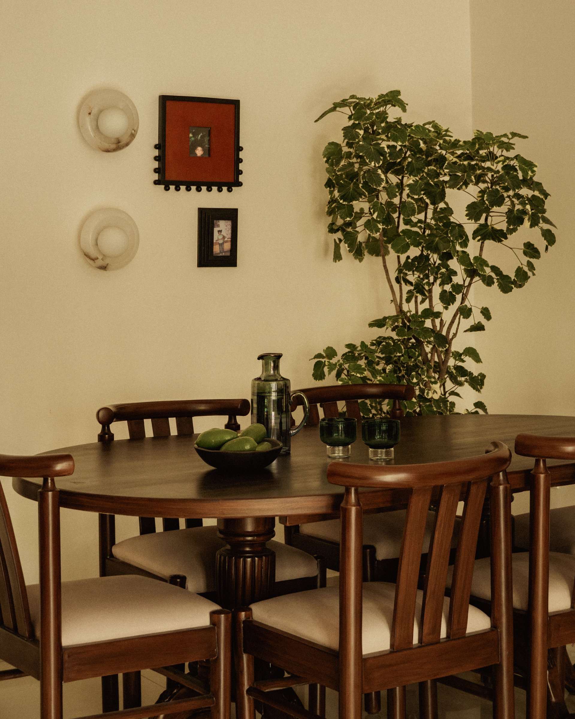 The dining area, anchored by a solid dark-wood pedestal table and chairs with curved backrests, with two alabaster wall discs above