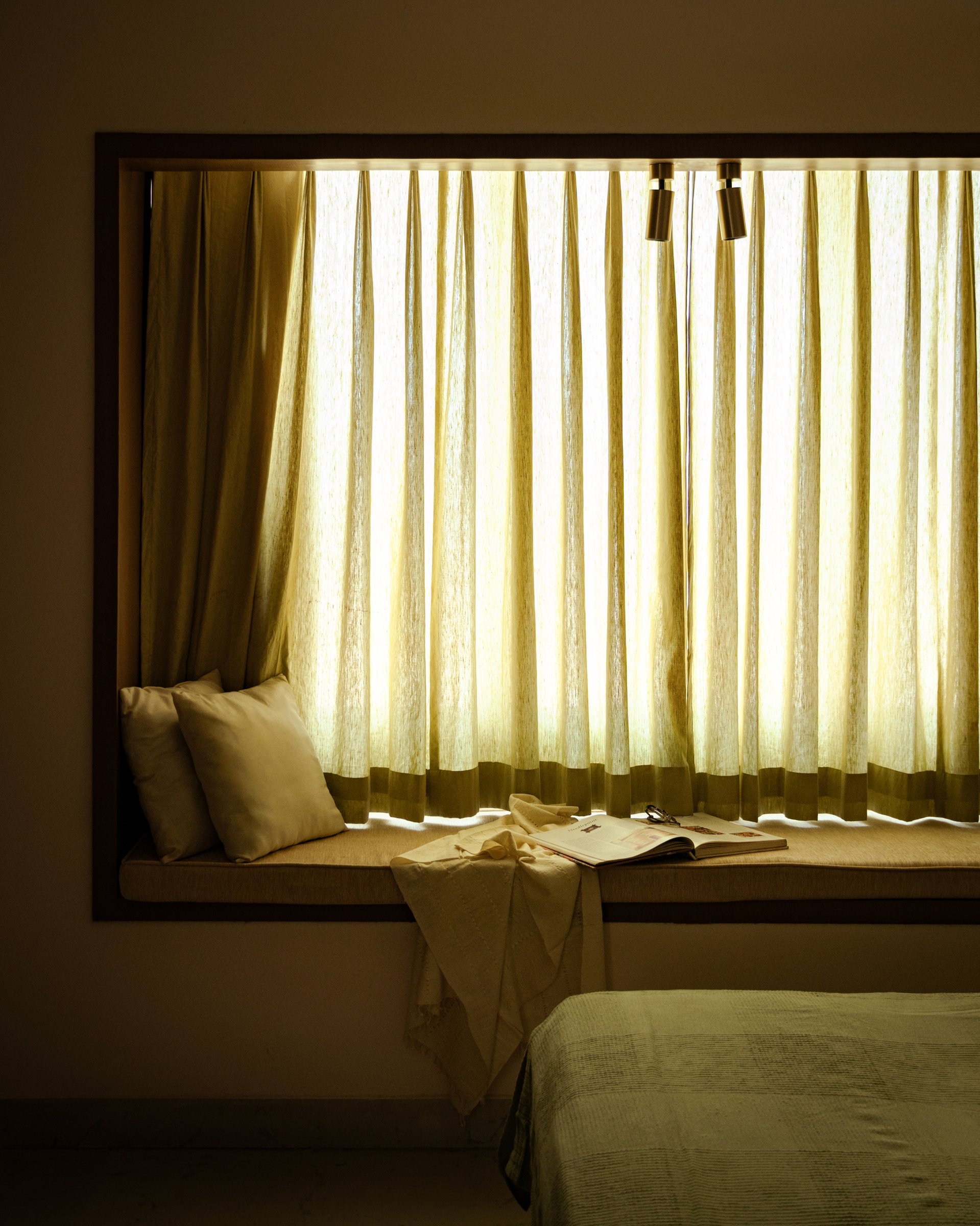 The window seat, upholstered in warm beige and softened by sheer golden linen curtains, functions as the home's quietest room