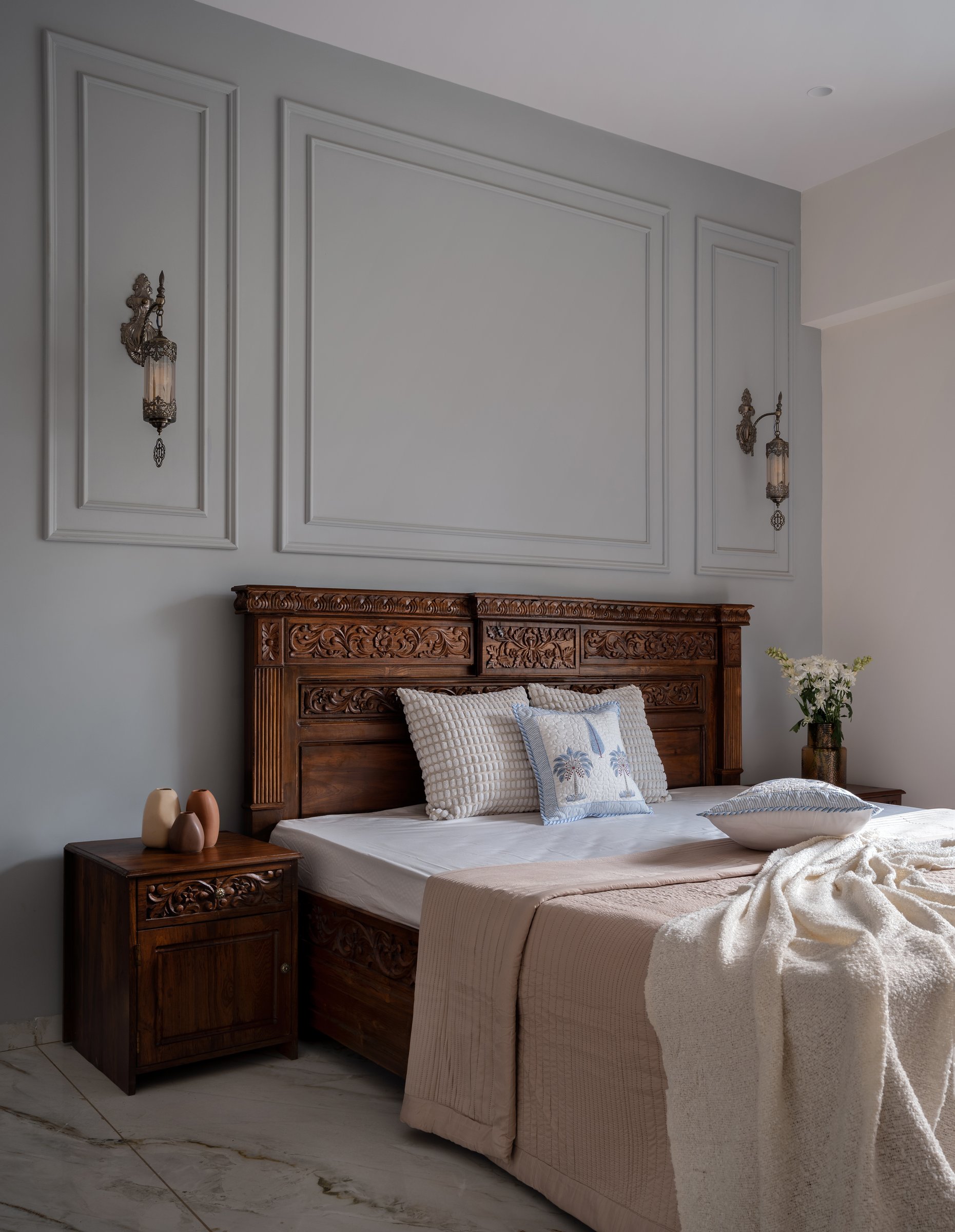 The guest bedroom, where a pale grey wall articulated with classical panel moulding frames another carved teak bed