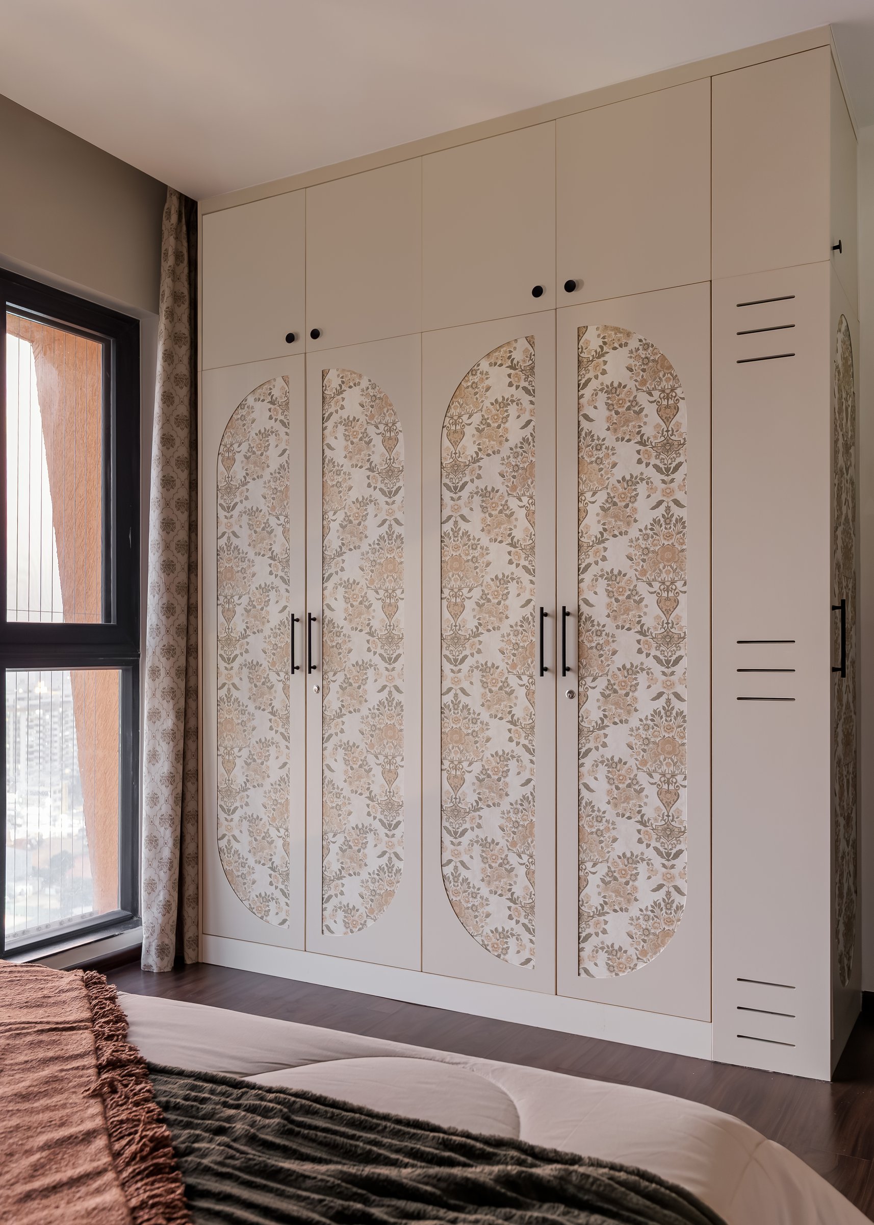 The wardrobe wall, its oval botanical-motif inserts carrying the room's ornament while the joinery recedes