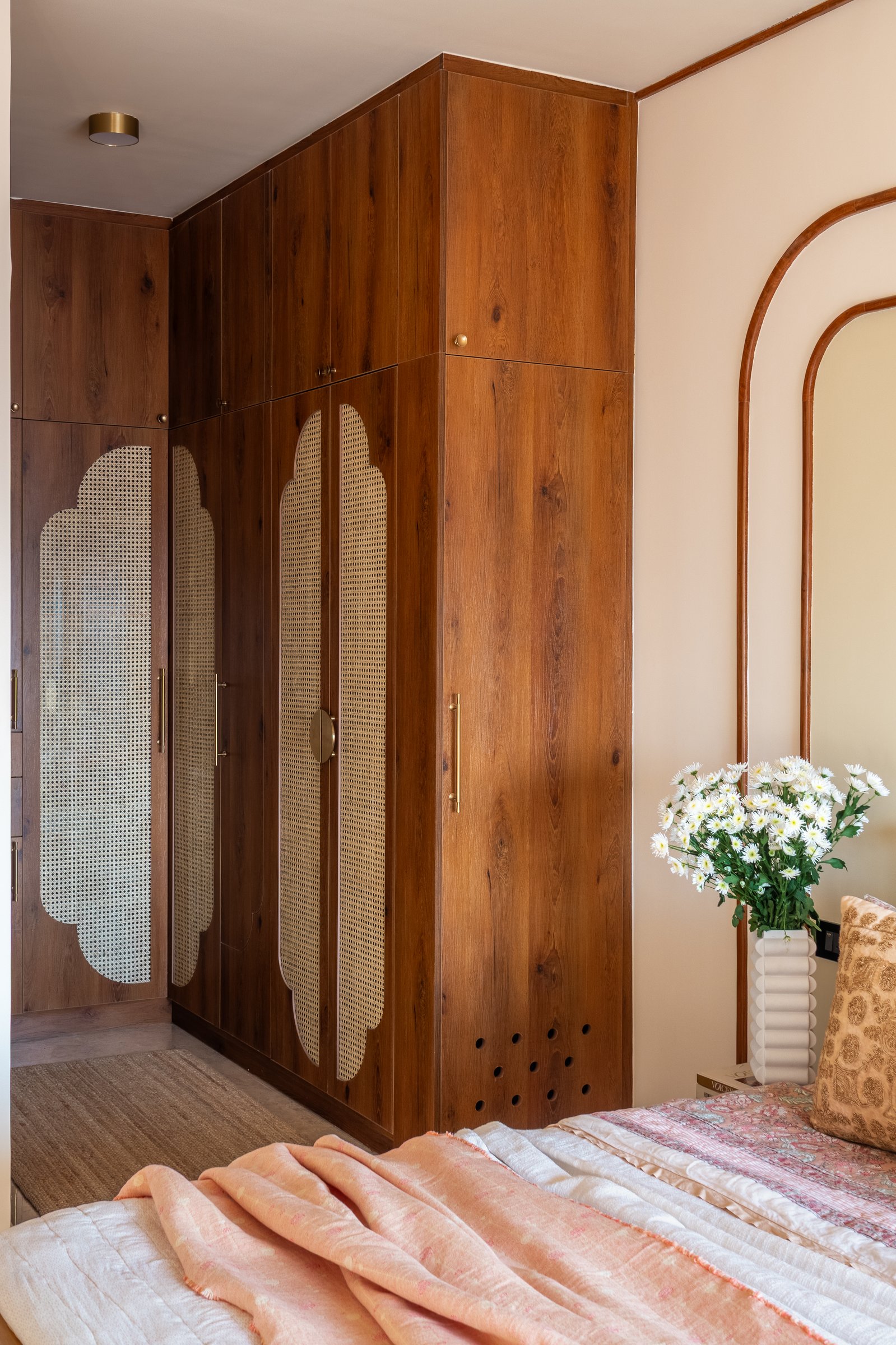 The master bedroom wardrobe, where scalloped cane-woven panels set into warm-toned doors read as architecture rather than joinery