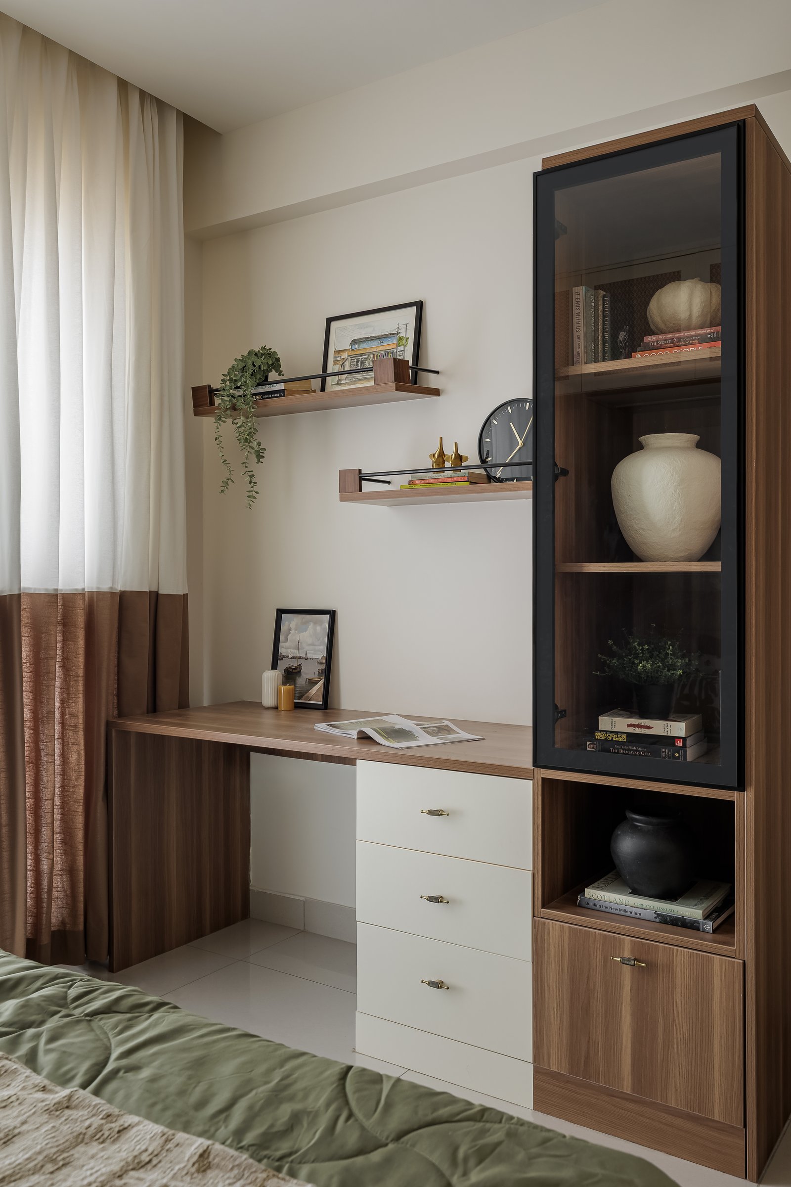 The study corner, its warm timber desk paired with a black-framed glass display cabinet and floating shelves