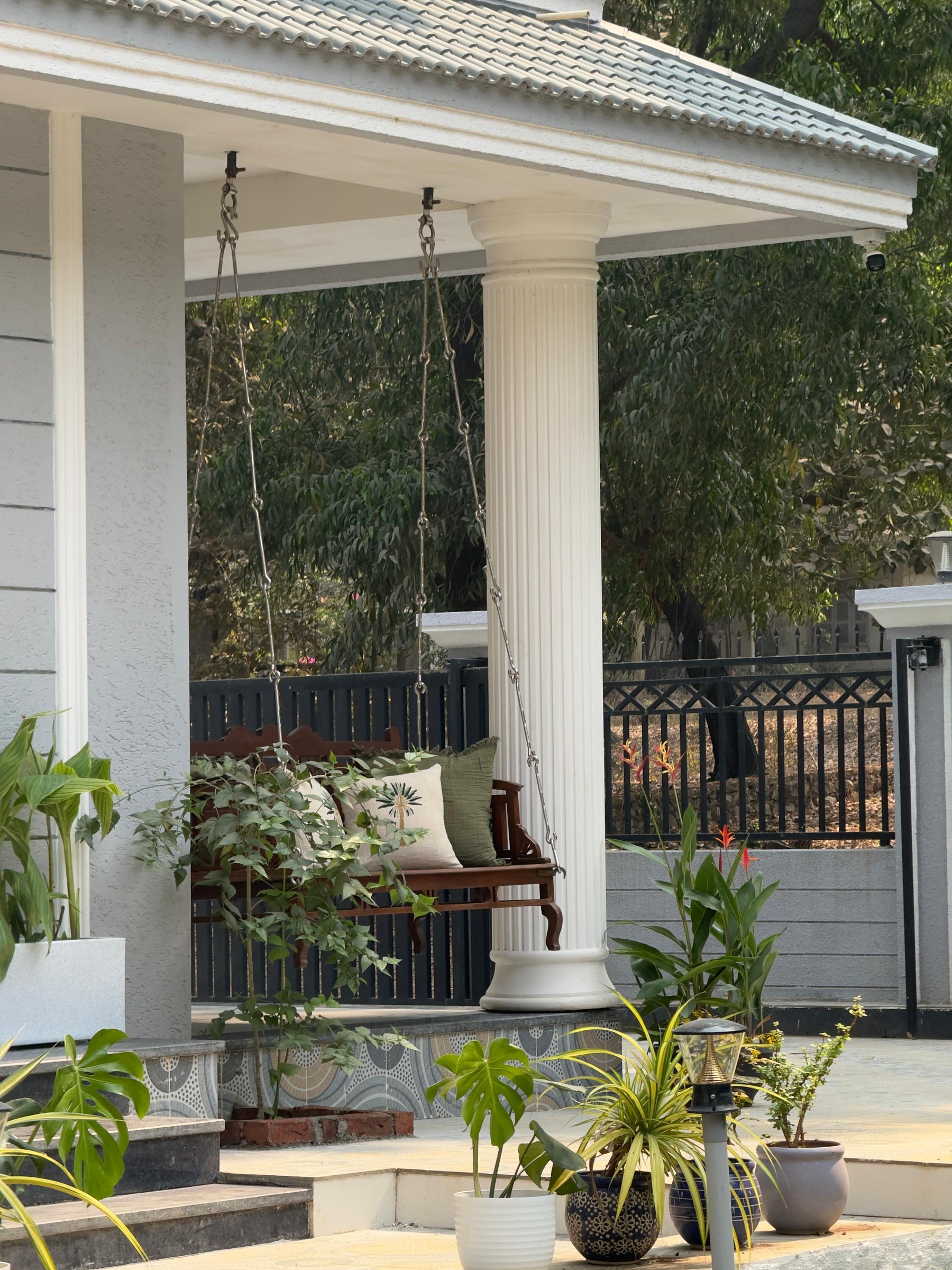 The carved teak swing between fluted columns, drawn from the Kerala oonjal tradition