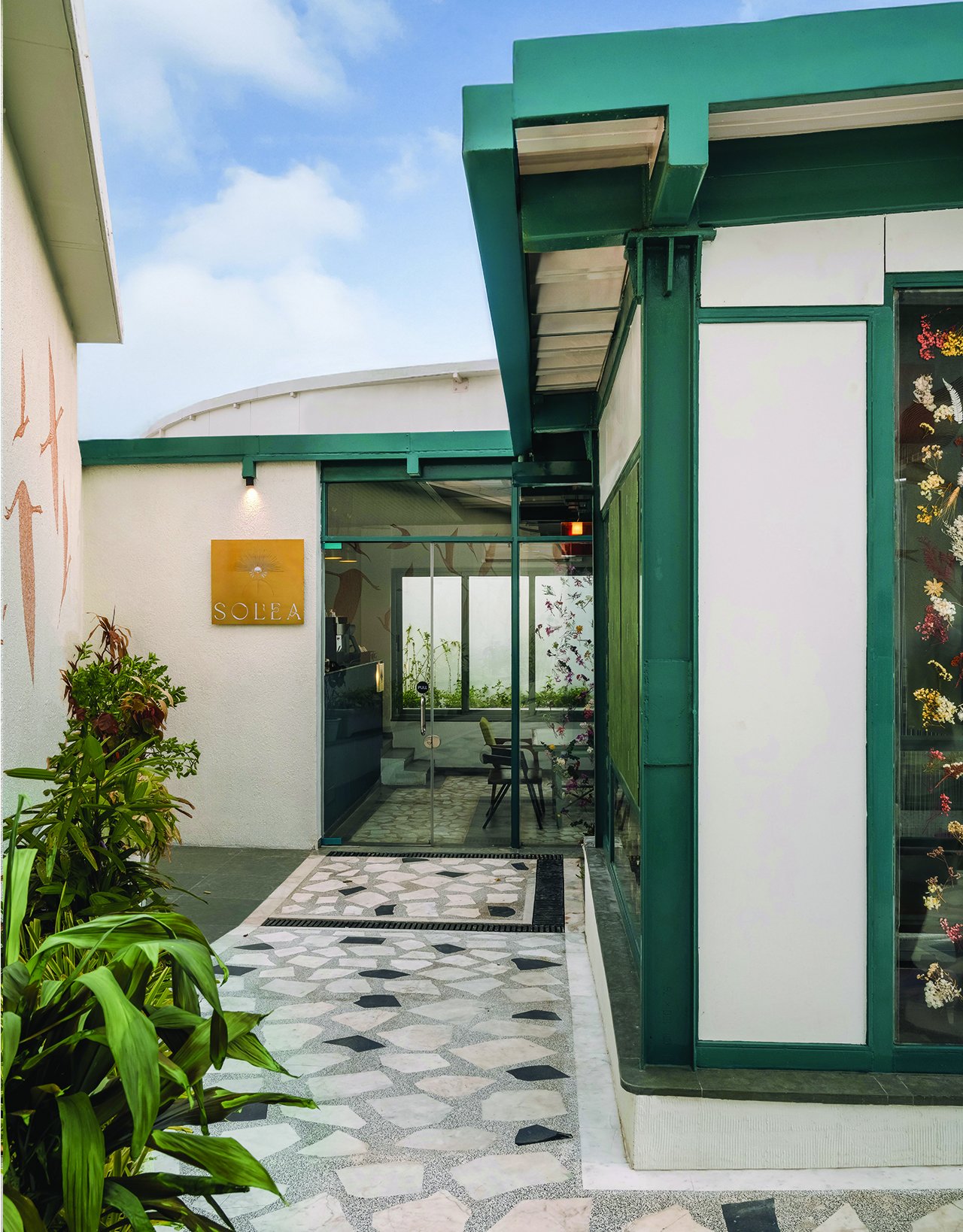 The threshold, where a crazy-paved marble walkway meets the tealed steel-and-glass shell of the café