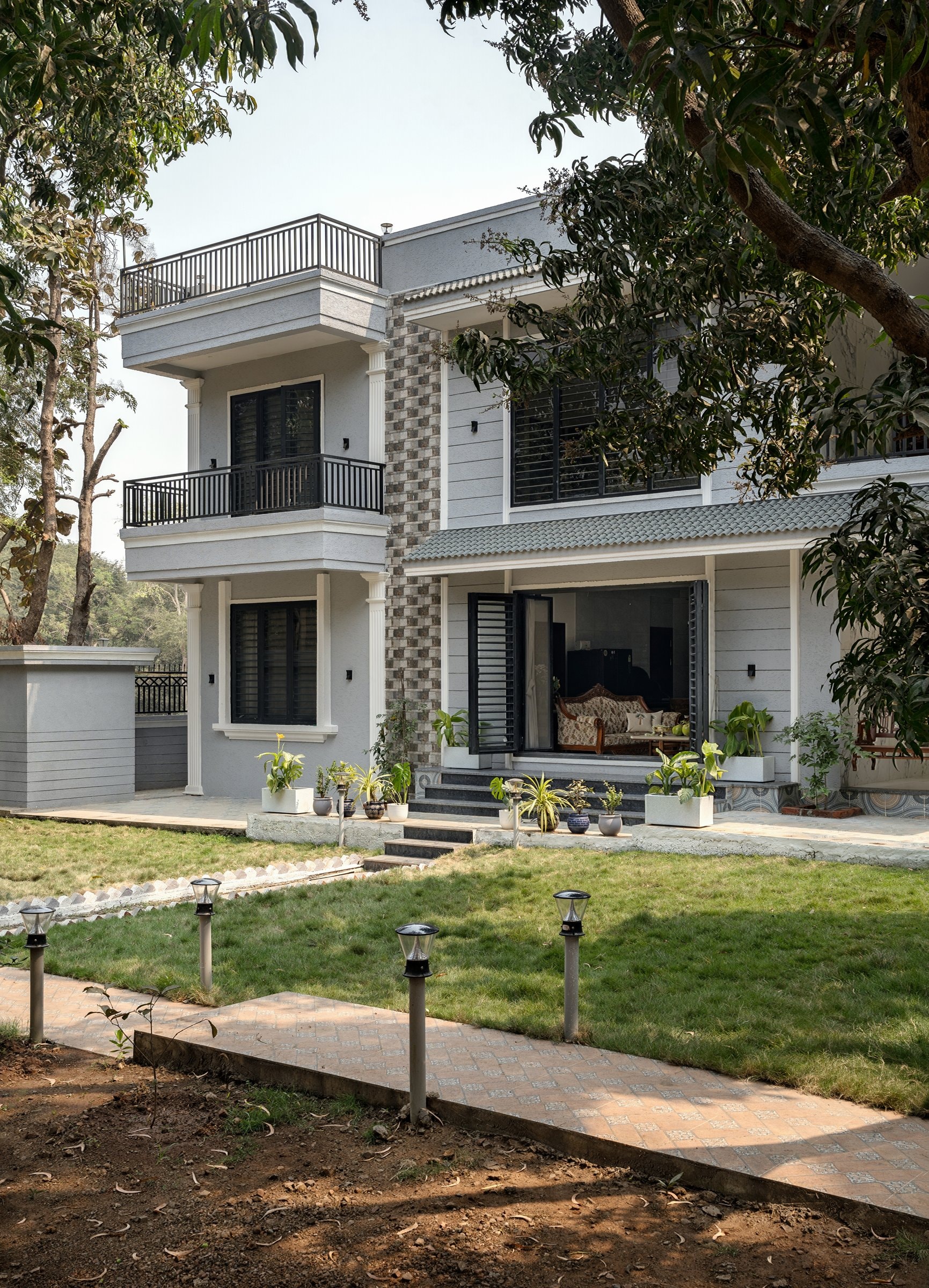 The garden elevation, where a tiled porch canopy shelters the living volume and a cantilevered balcony floats above