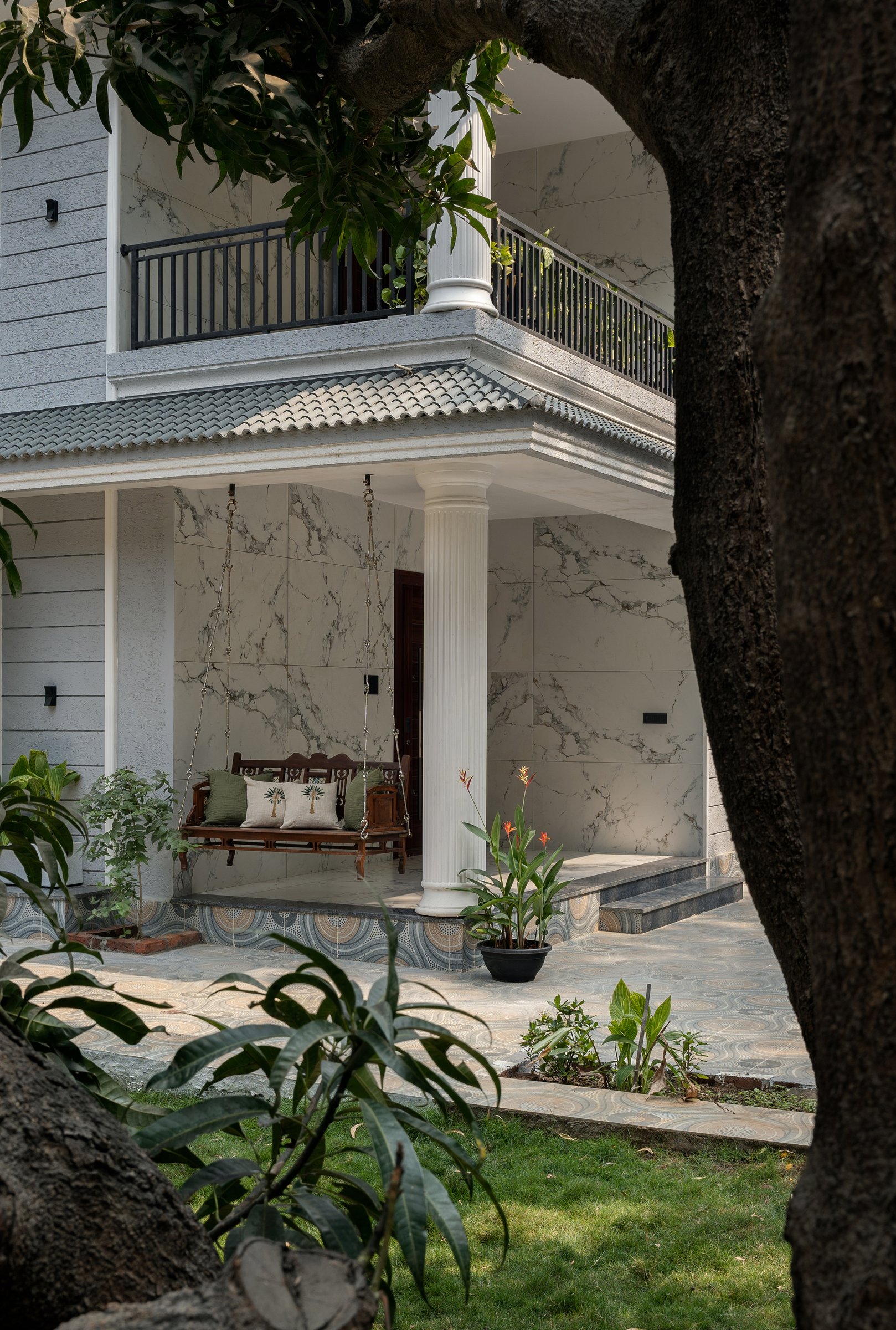 The porch framed by a mature tree, revealing itself as a semi-enclosed room that slows arrival