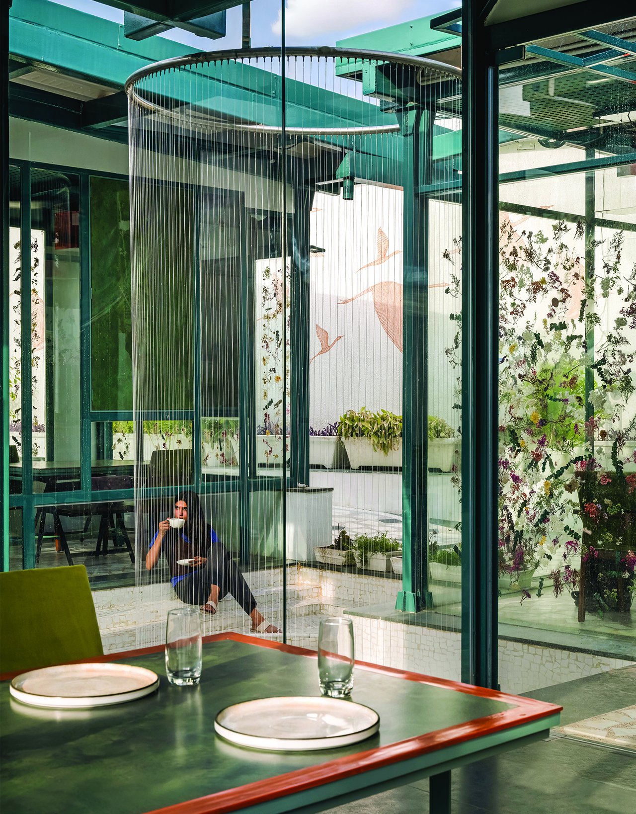 A view from a dining table toward the water court, where the crane mural reappears through the strand curtain