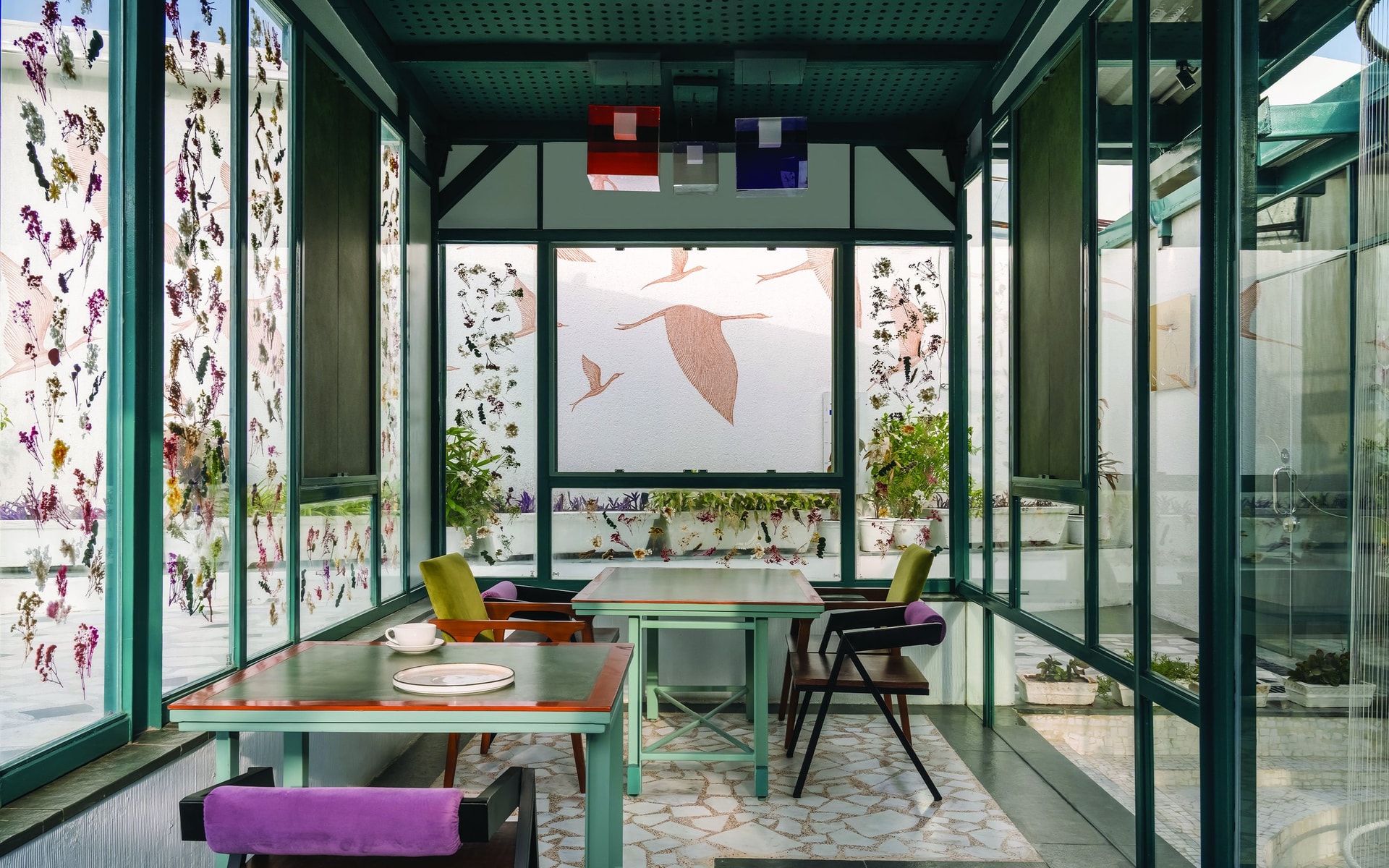 The glazed dining pavilion, where warm-topped tables meet chairs in mustard and lilac against walls of pressed-botanical glazing
