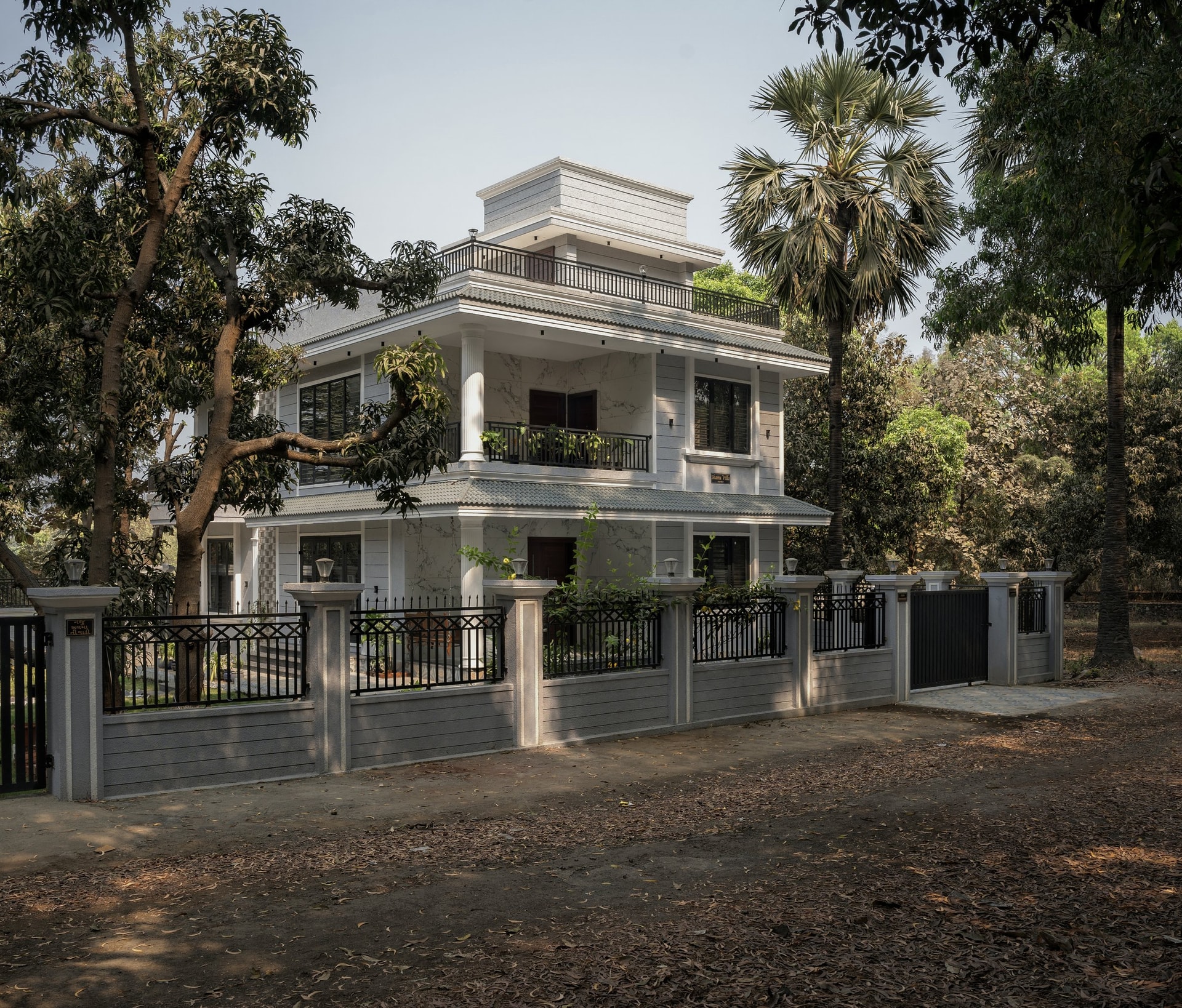 The villa seen from the compound gate, where fluted columns, a tiled eave and a marble-clad central bay set the neo-classical tone