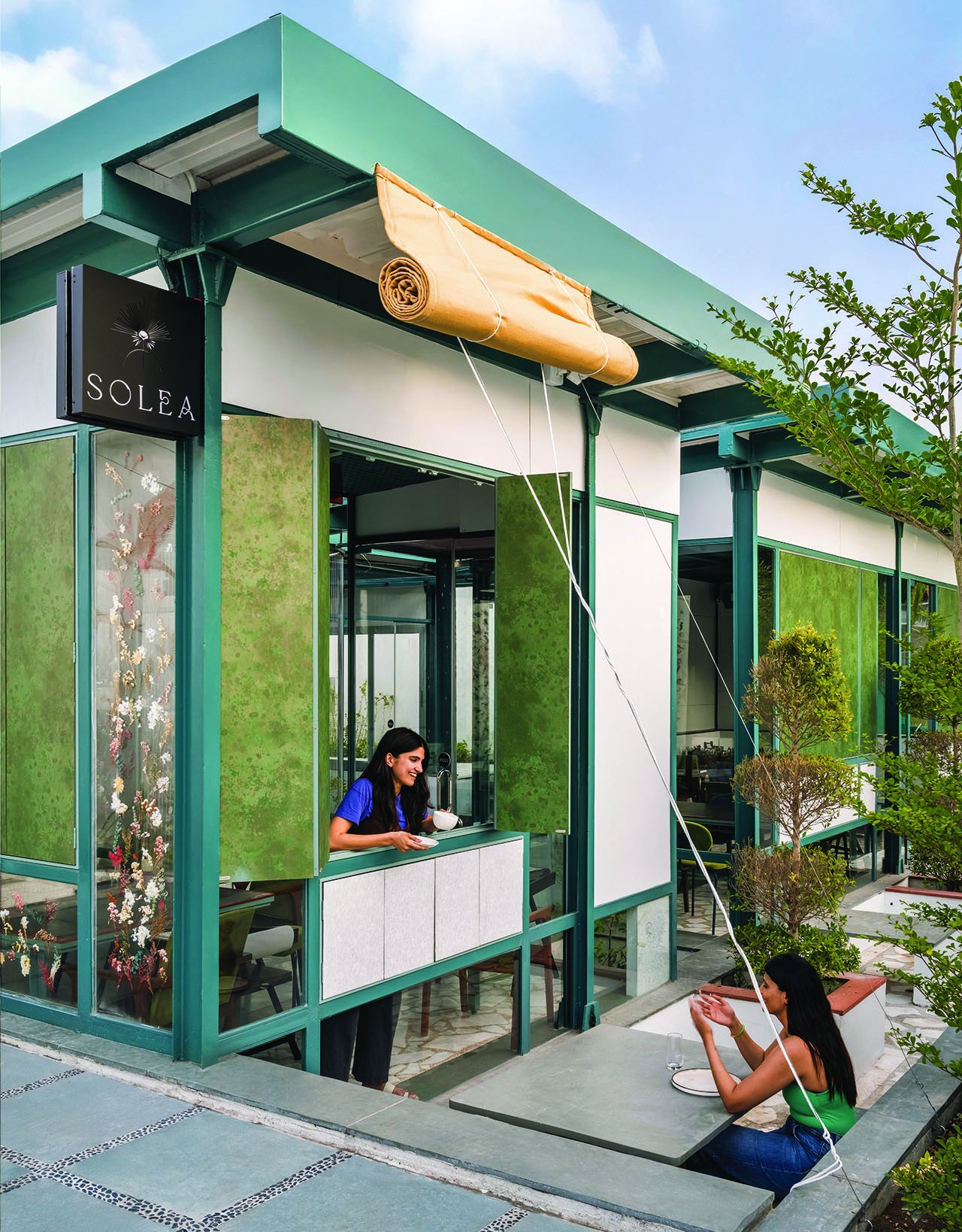 The façade, where tealed steel columns frame panels of green-tinted glass, pressed-botanical glazing, and an openable service window
