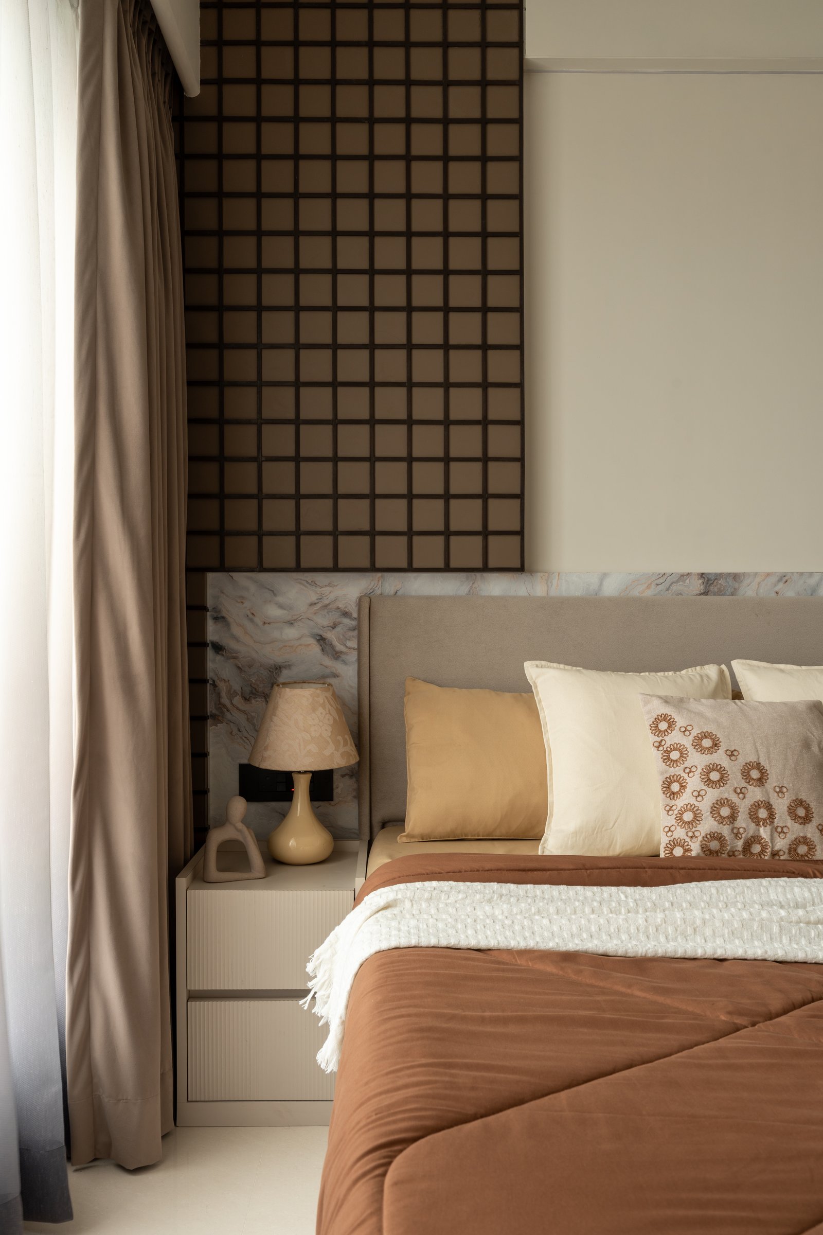 The bedside detail, with a fluted cabinet and single ceramic lamp against the warm stone band