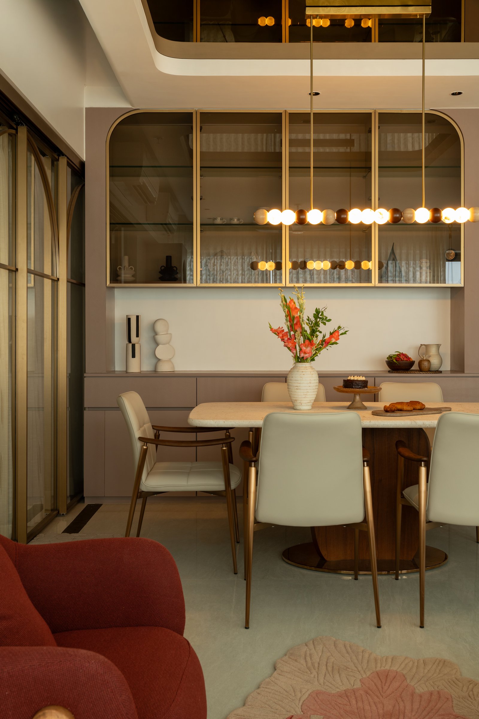 The arched glazed cabinets in slim bronze framing, holding ceramics and objects behind the dining table