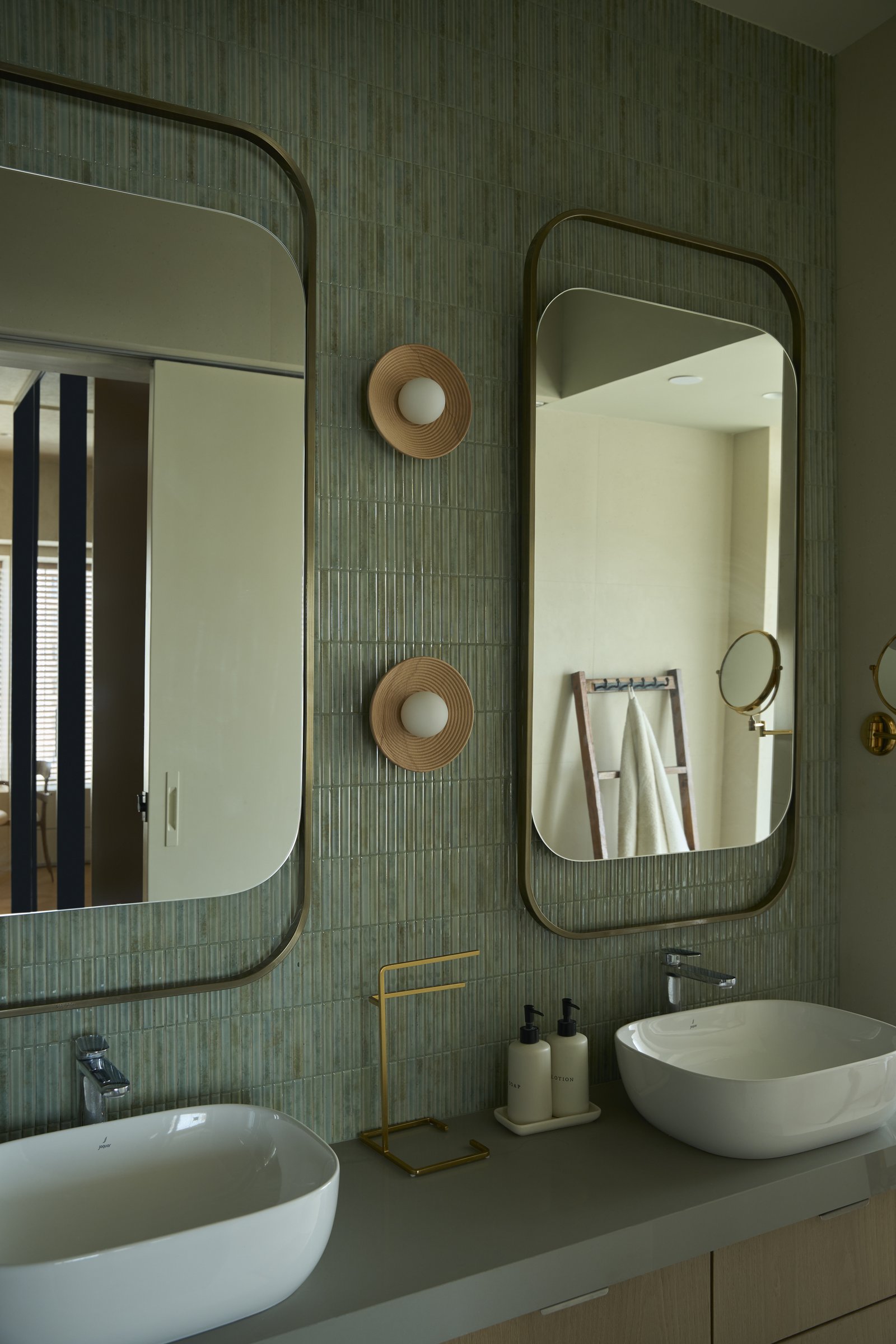 The principal bathroom, where ribbed sage-toned tiles meet brass-framed mirrors and fluted wall sconces