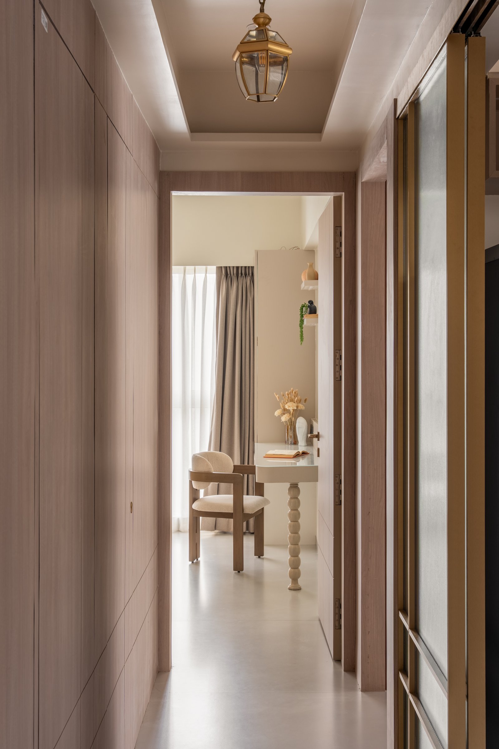 The passage, lined with wood-grain wardrobes and fluted-glass doors, lit by a lantern-style pendant that frames a view of the study beyond