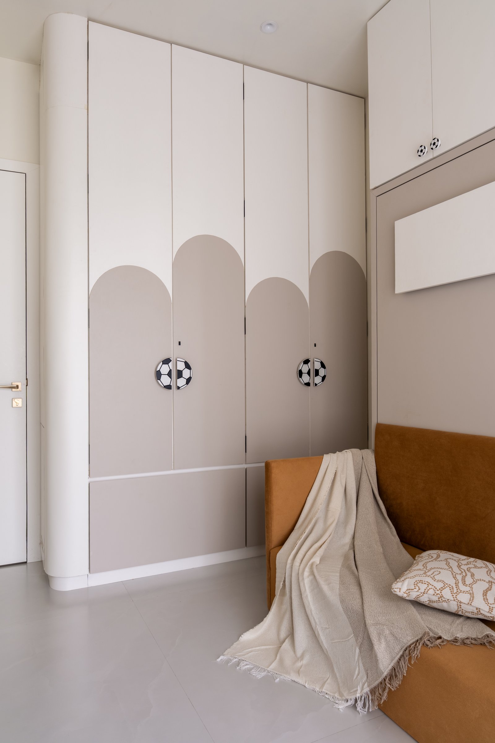 The son's wardrobe wall, where muted arches and football-motif handles translate the child's interests into architectural pattern