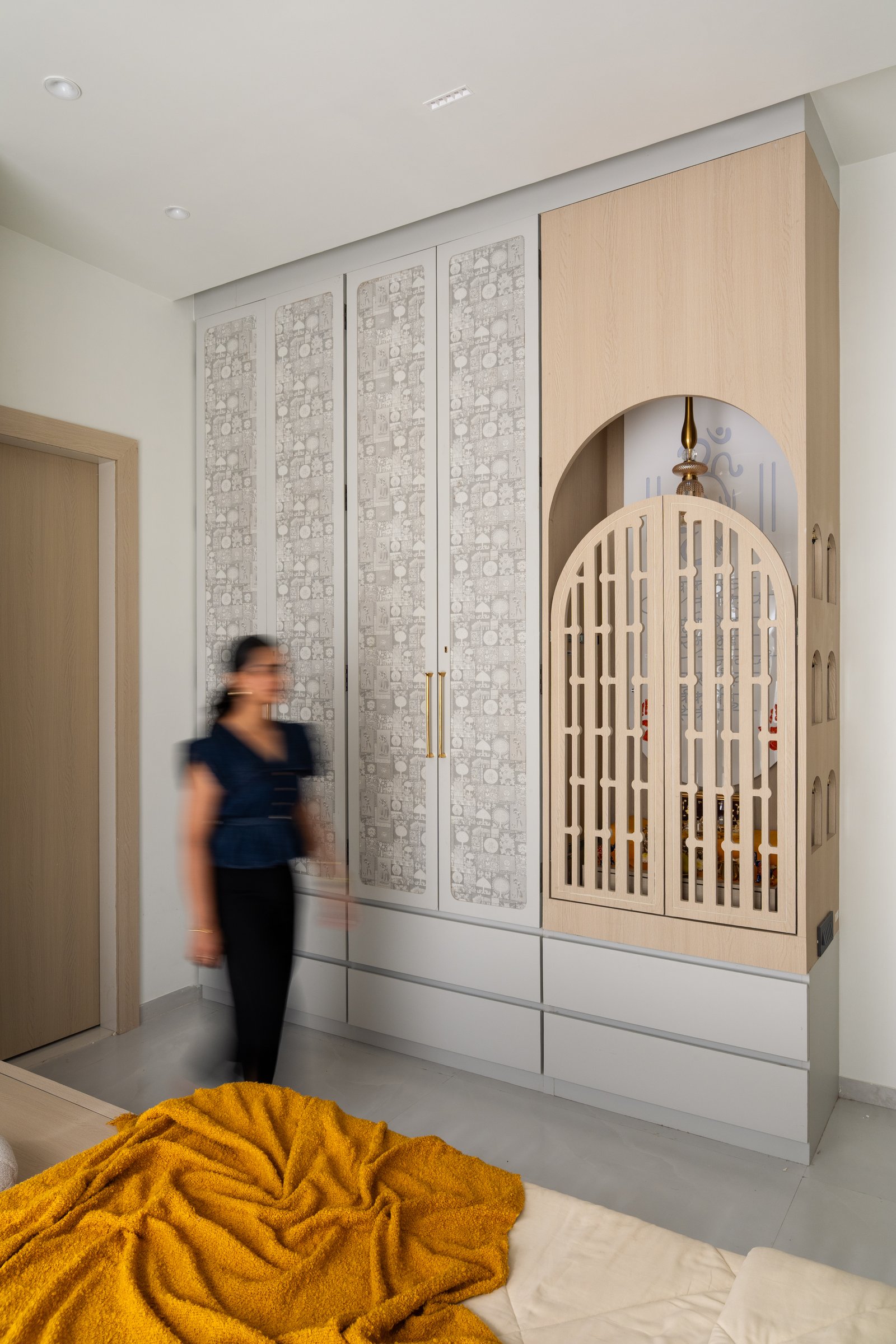 The pooja unit, its arched screen doors in blond wood flanked by cabinetry with softly patterned wallpaper insets