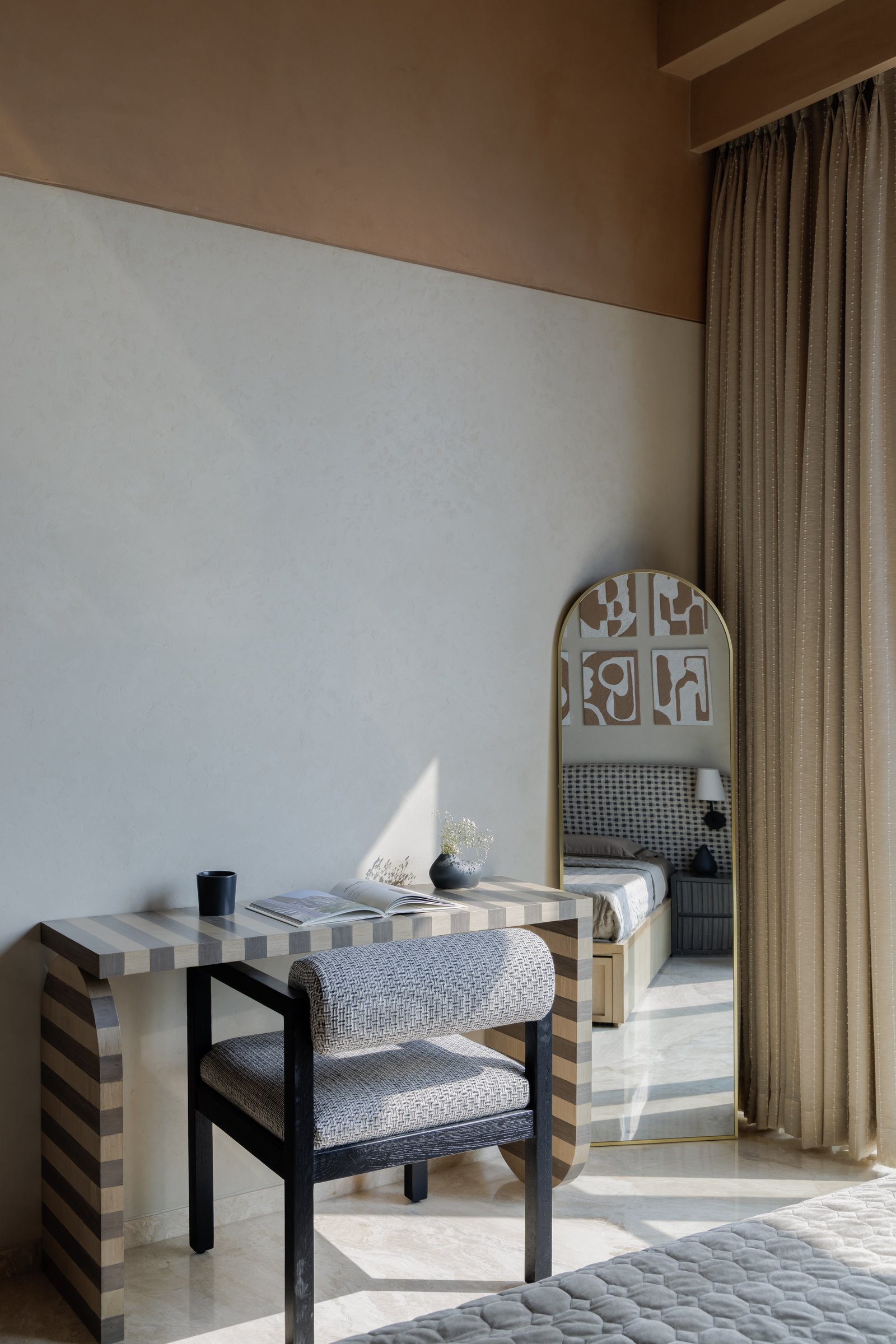 A writing corner within the guest bedroom, where a striped desk and an arched brass-framed mirror are caught in soft daylight
