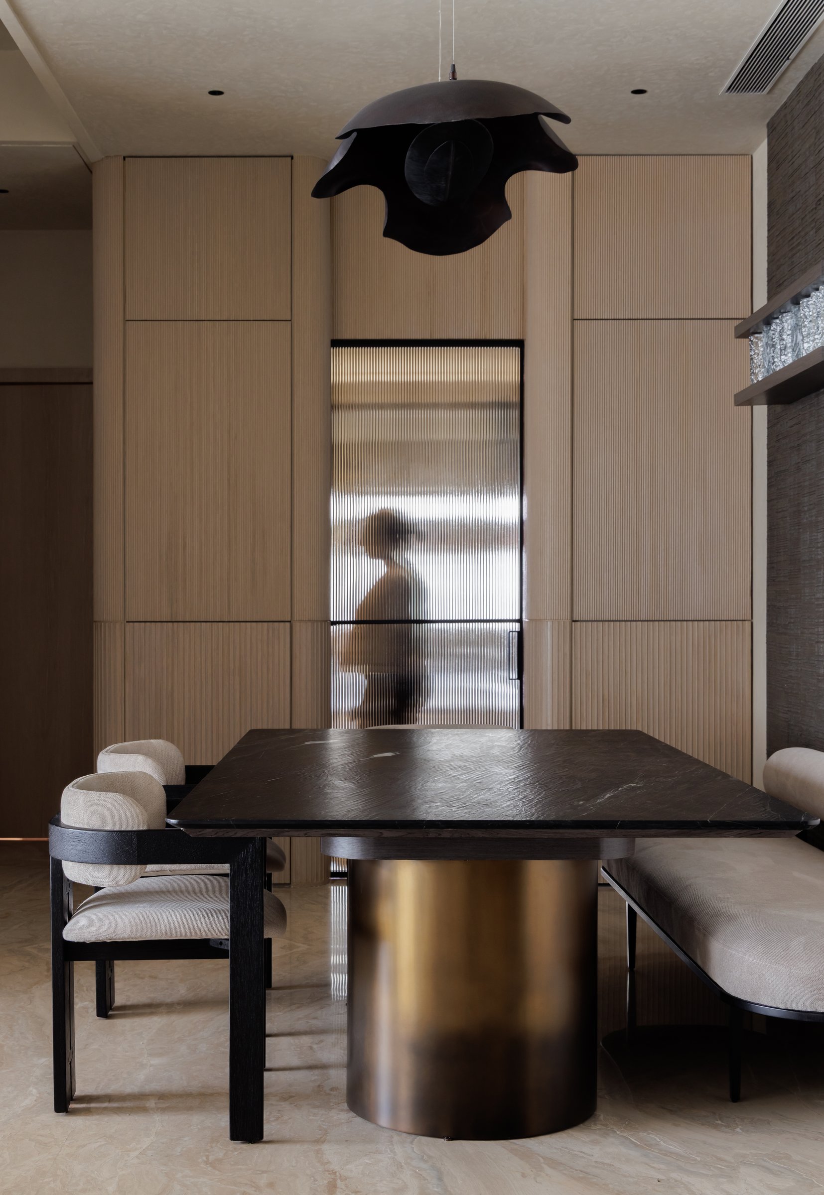 The dining area, where a dark stone tabletop rests on a single brushed brushed-bronze cylindrical base beneath a sculptural pendant