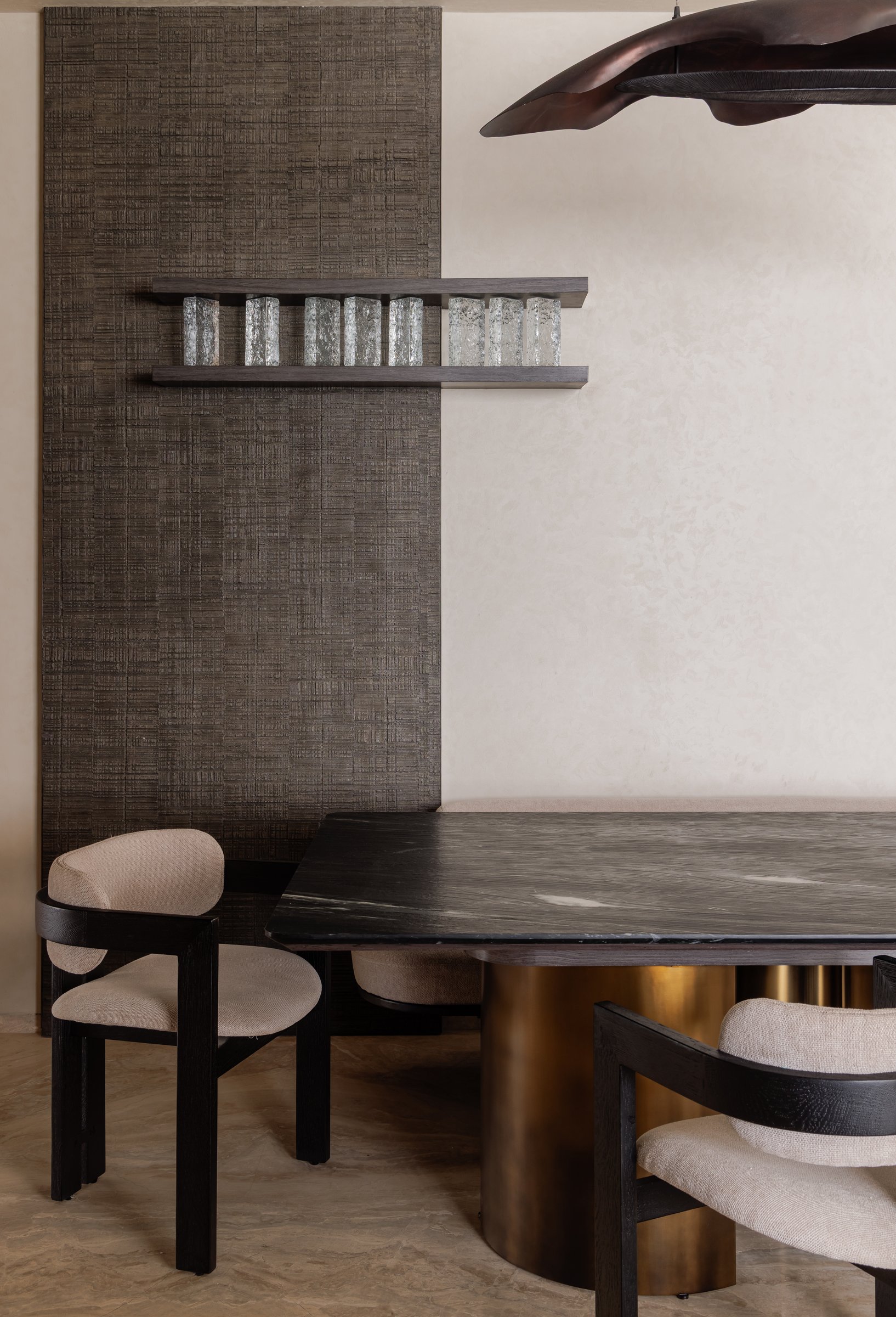 A closer view of the dining setting, where a textile-panelled wall carries a slim shelf lined with small crystalline objects