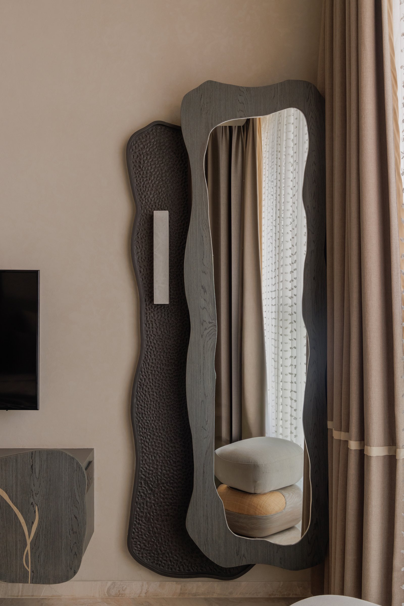 A wall composition of undulating mirror and hammered metal panel, paired with a small pale marble sconce