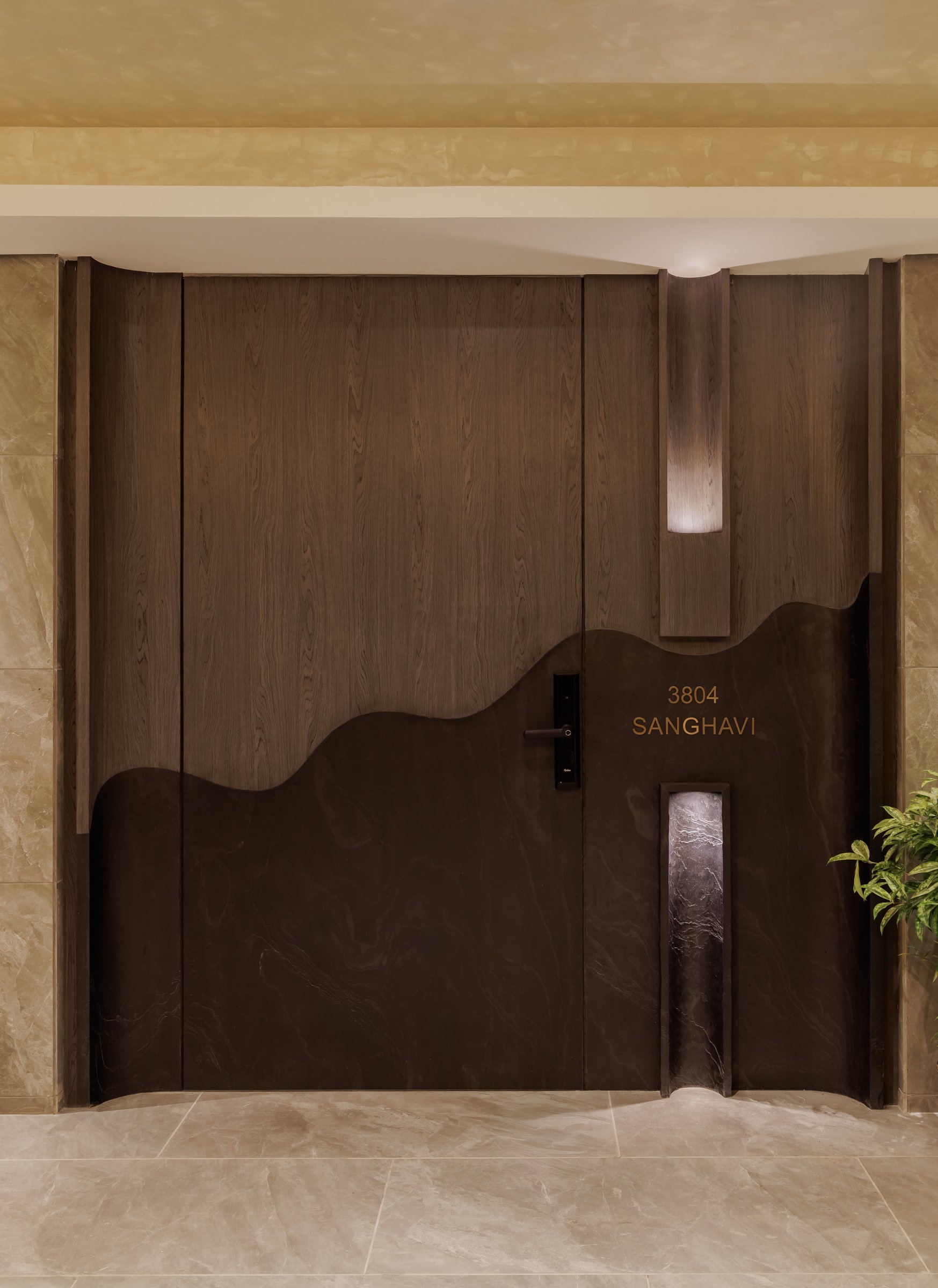 The entrance, where a smoked oak door with an undulating cut-line and a bronze-inlaid family name sets the tone before the home begins
