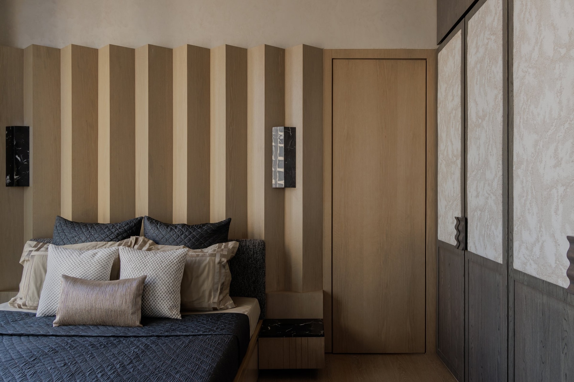 The primary bedroom, where alternating pale and darker oak panels with a scalloped upper edge form the headboard wall