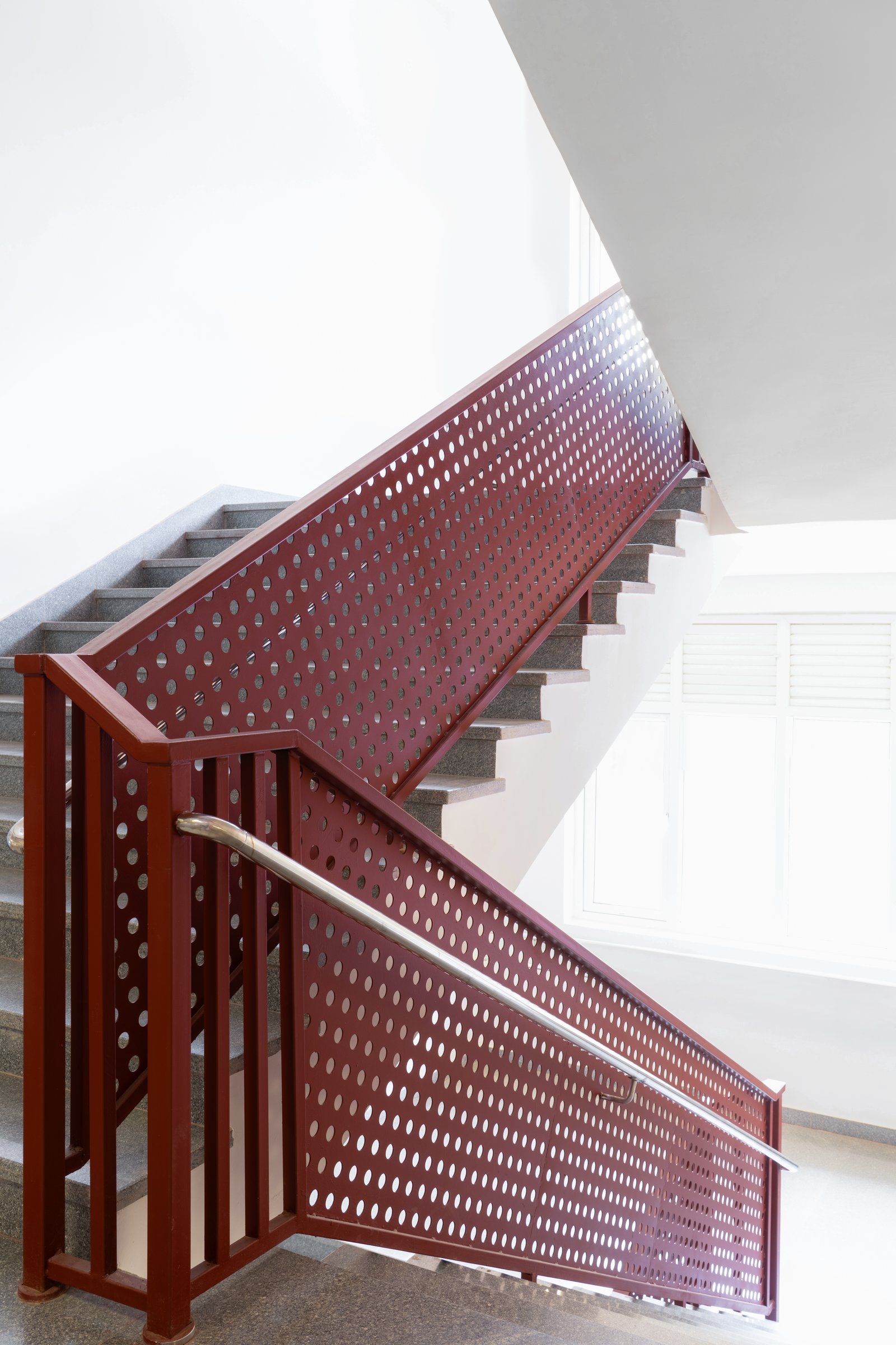 The stair core, where a perforated deep red steel balustrade turns a safety element into the school's most recognisable gesture