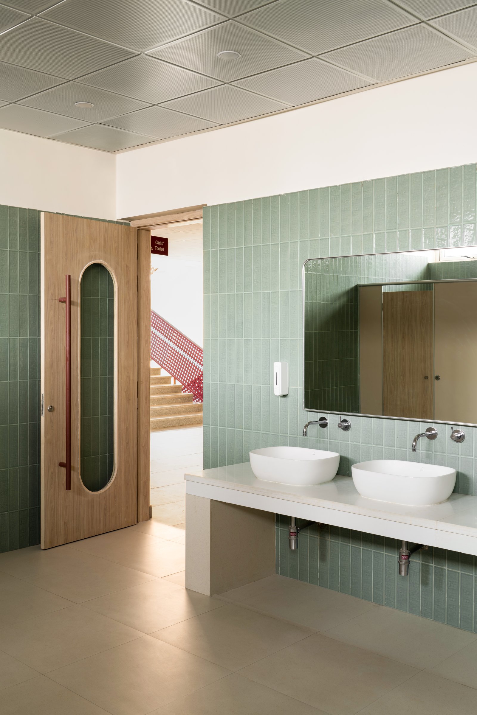 The washroom, where sage-green stacked tiles and a capsule-cutout oak door distil the campus vocabulary into a small utilitarian moment